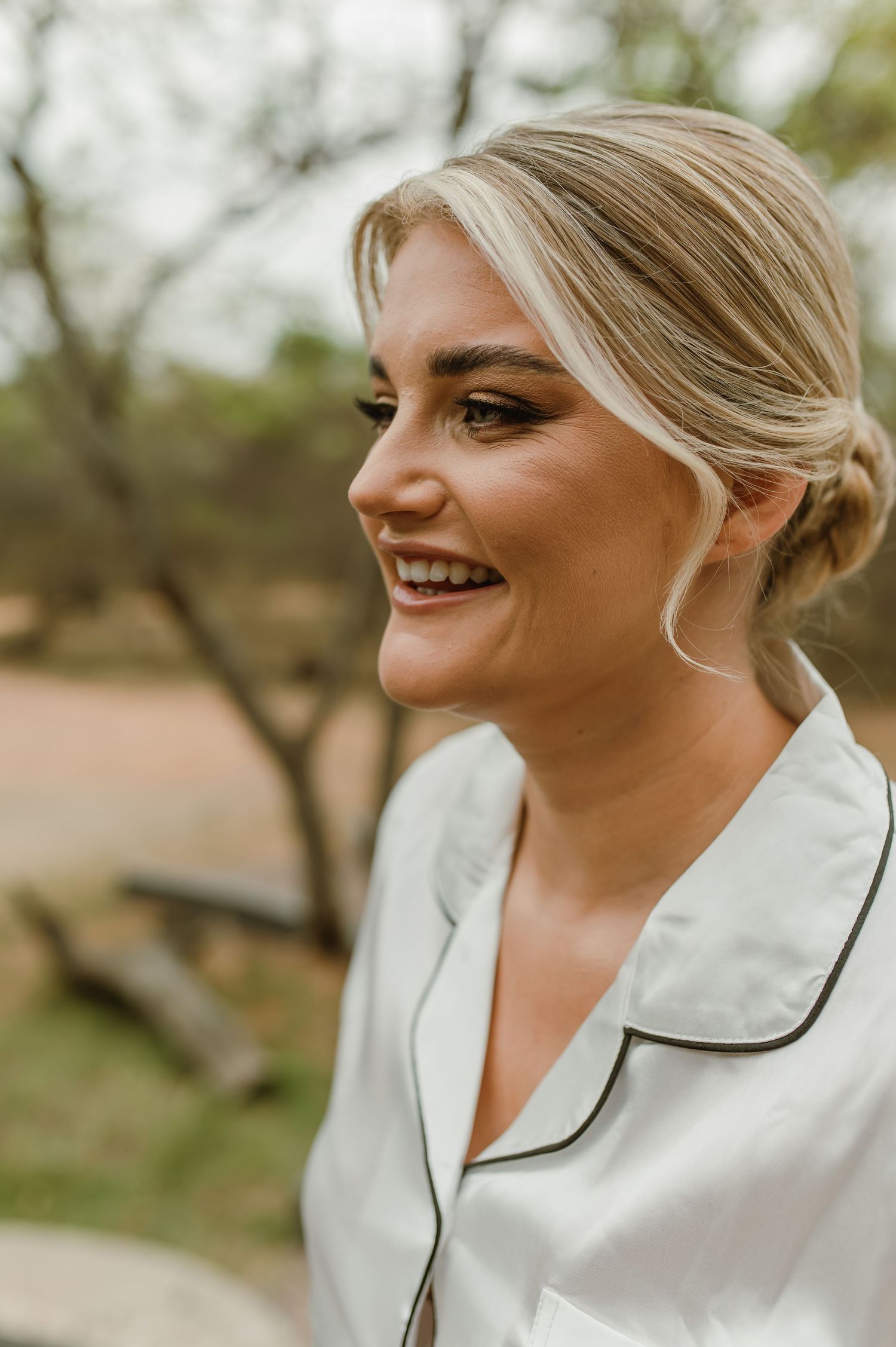 Close up profile view of person in white silk pajamas smiling outdoors.