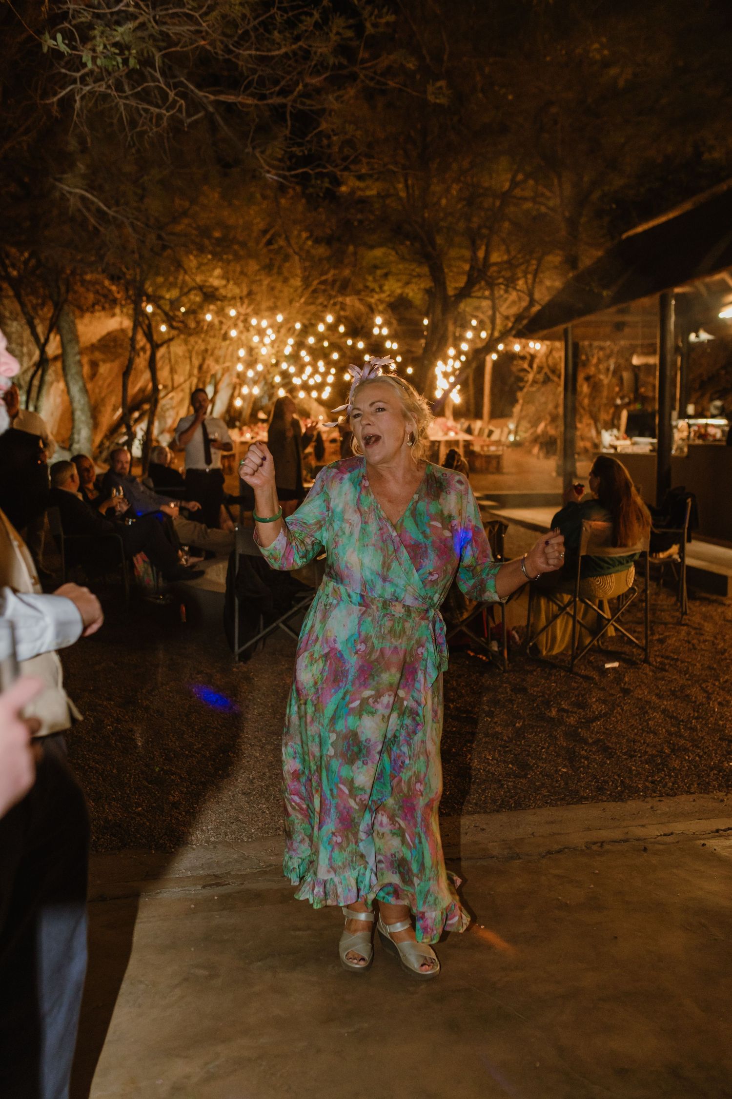 People dancing and celebrating at a nighttime wedding reception under string lights.