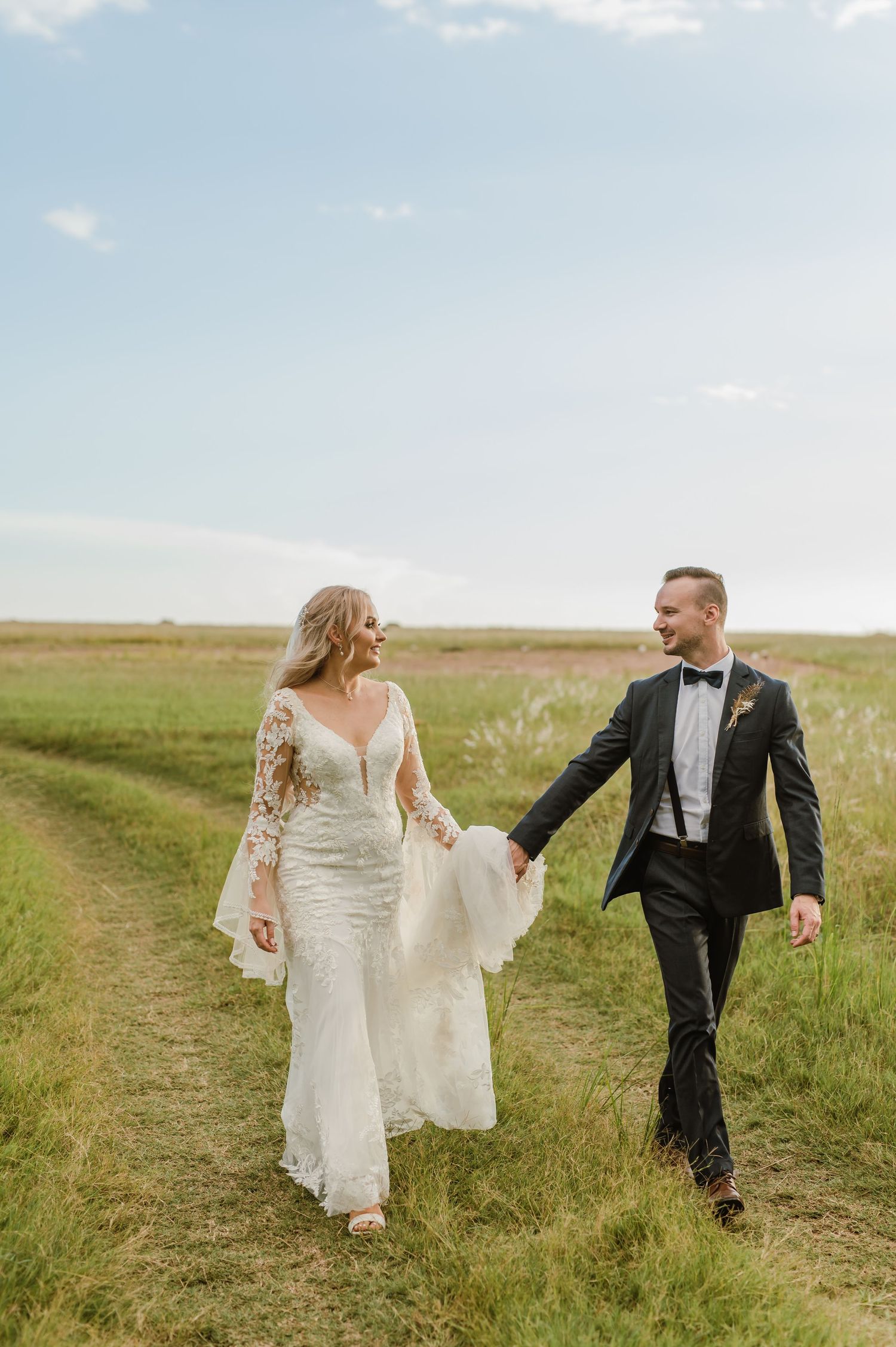 Wedding couple walking hand in hand through a sunny green field.