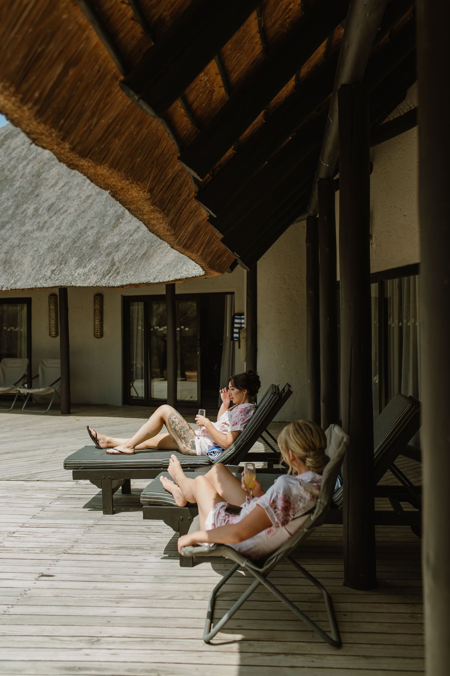 A relaxing scene on a covered porch with lounge chairs and thatched roof overhead.