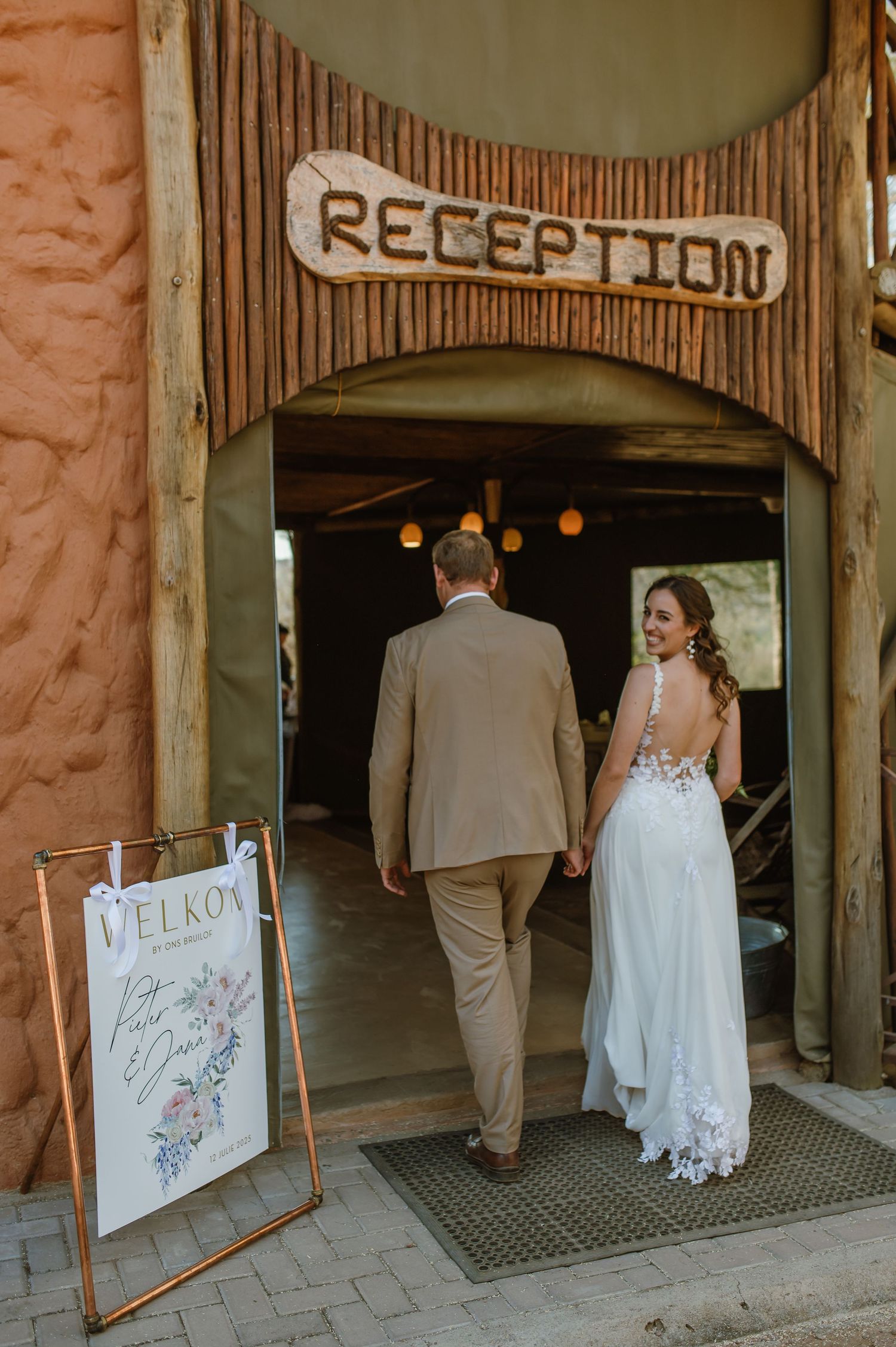 Couple walking through rustic archway entrance at outdoor venue.