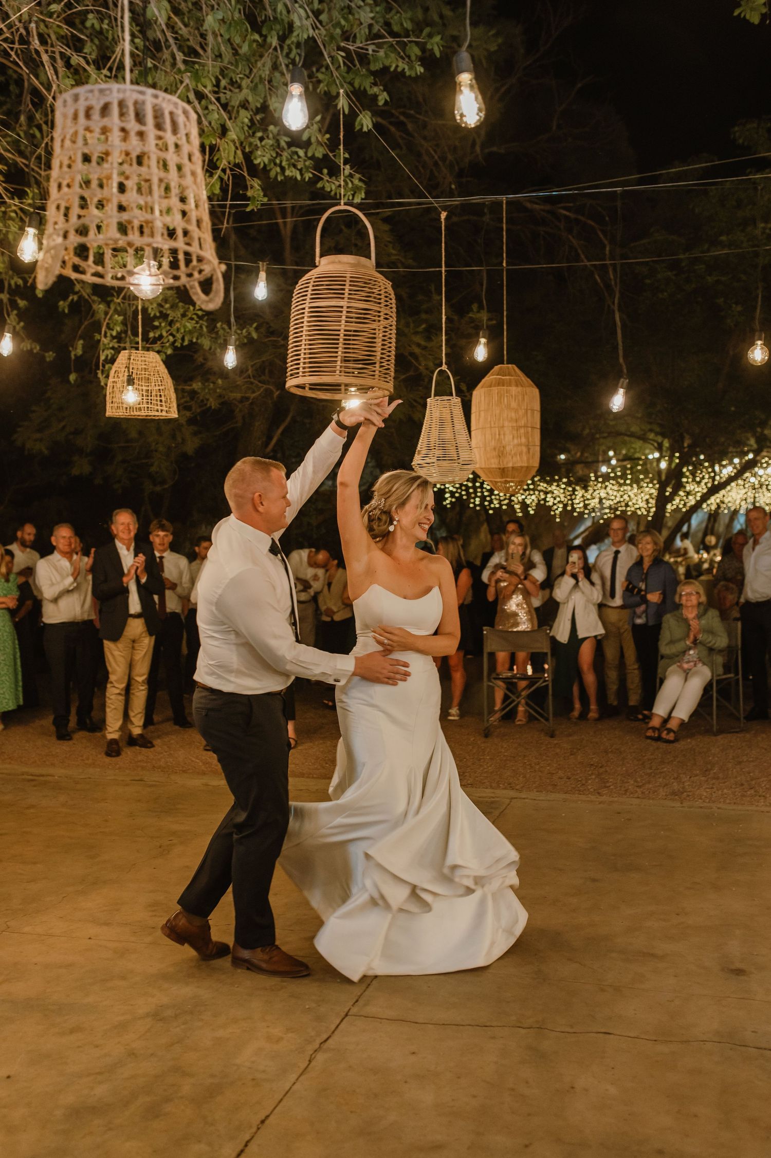 Romantic first dance under rustic wicker lanterns and string lights at nighttime outdoor reception.