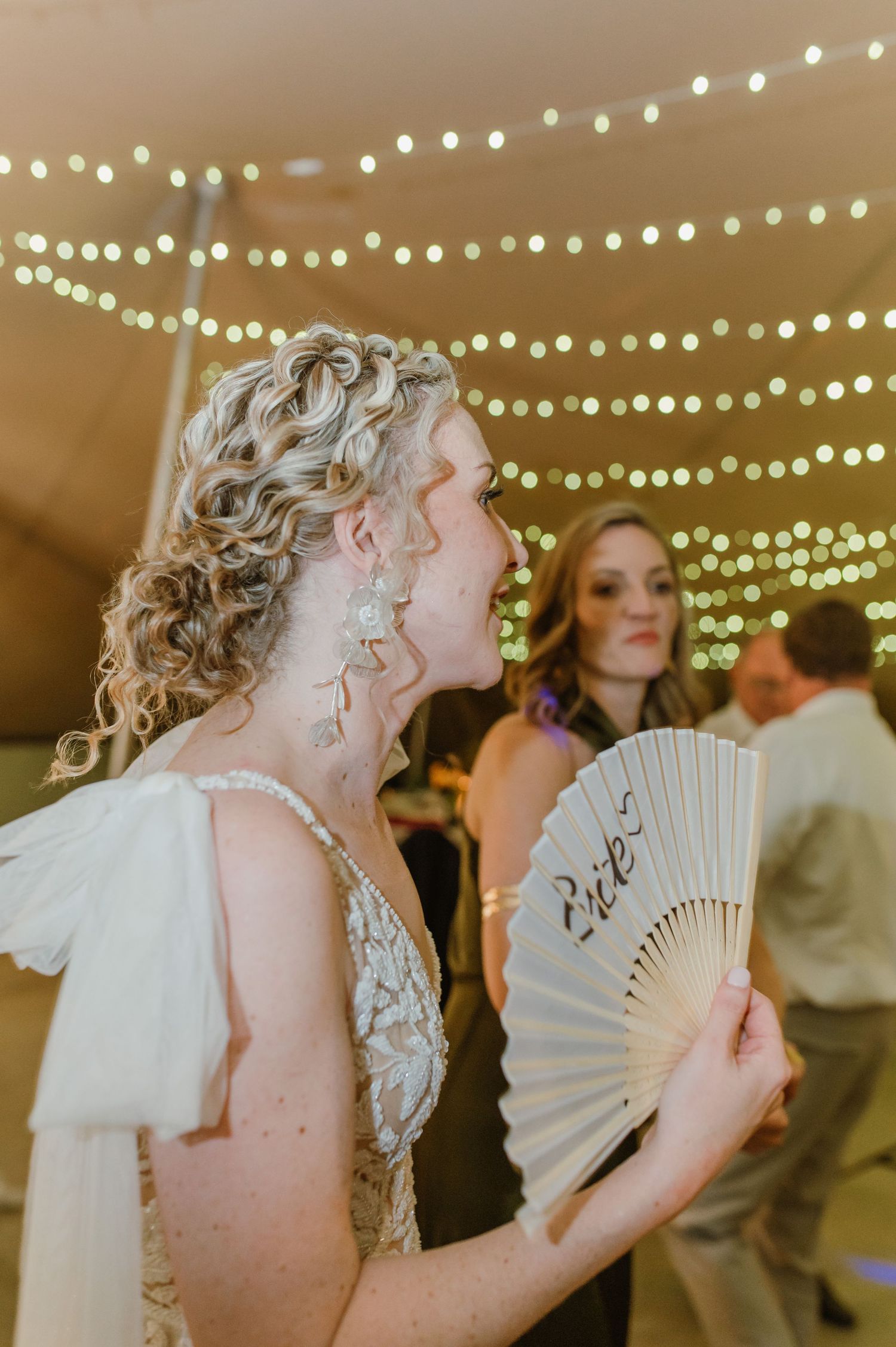 Person in white dress holding a decorative fan while dancing under string lights.