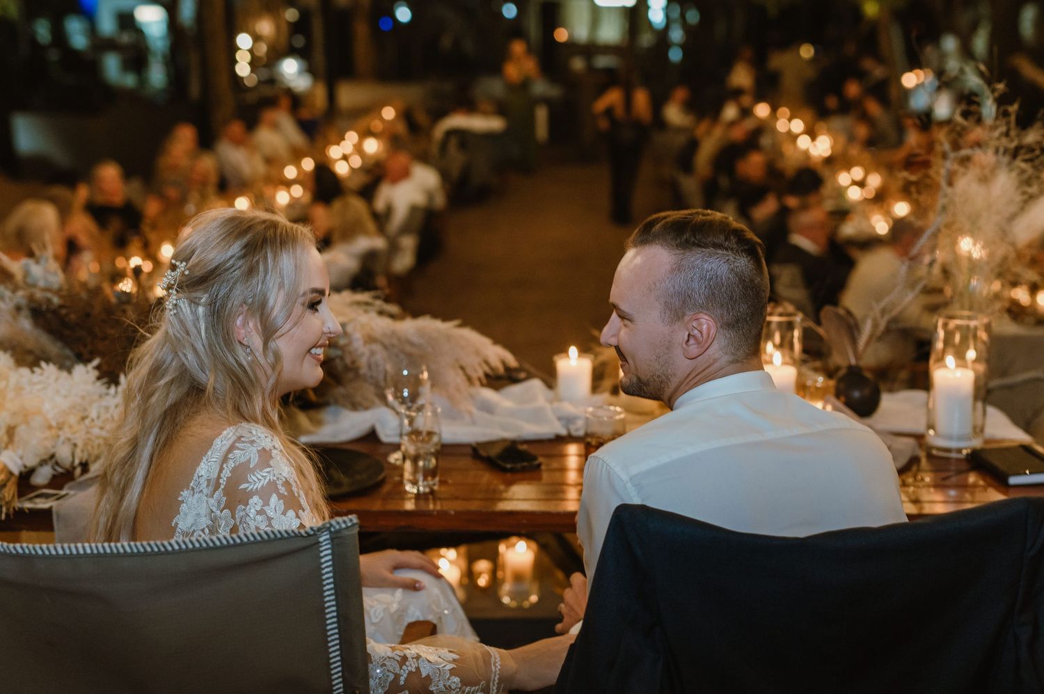 Couple seated at candlelit reception table during outdoor evening celebration.