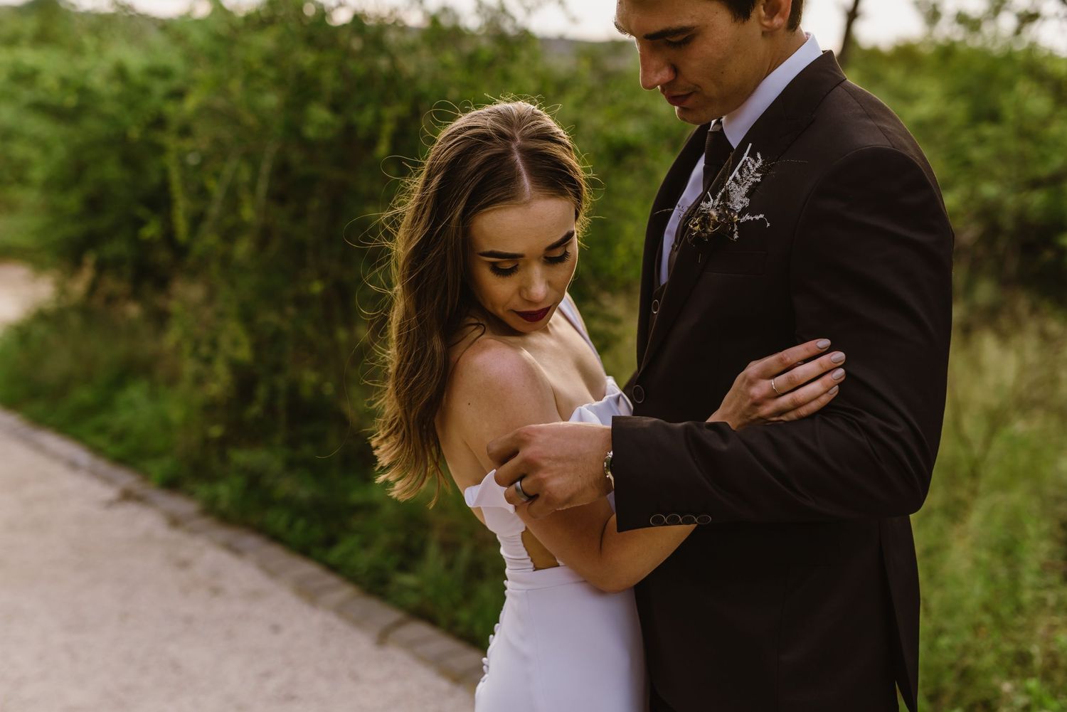 Newlyweds embrace tenderly on a rustic path during their wedding photoshoot.