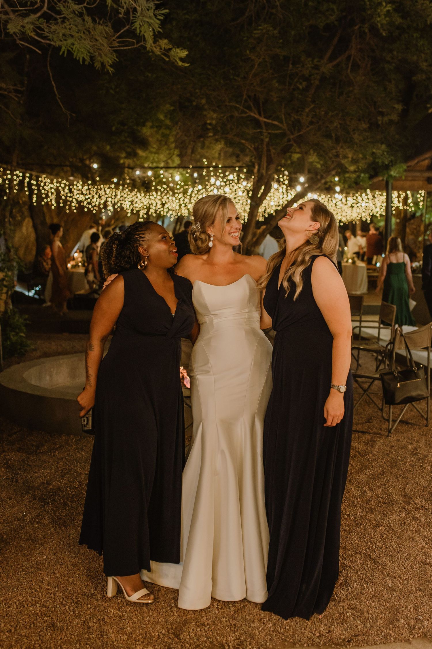 Wedding party members in black and white attire celebrate together on a rustic outdoor dance floor.