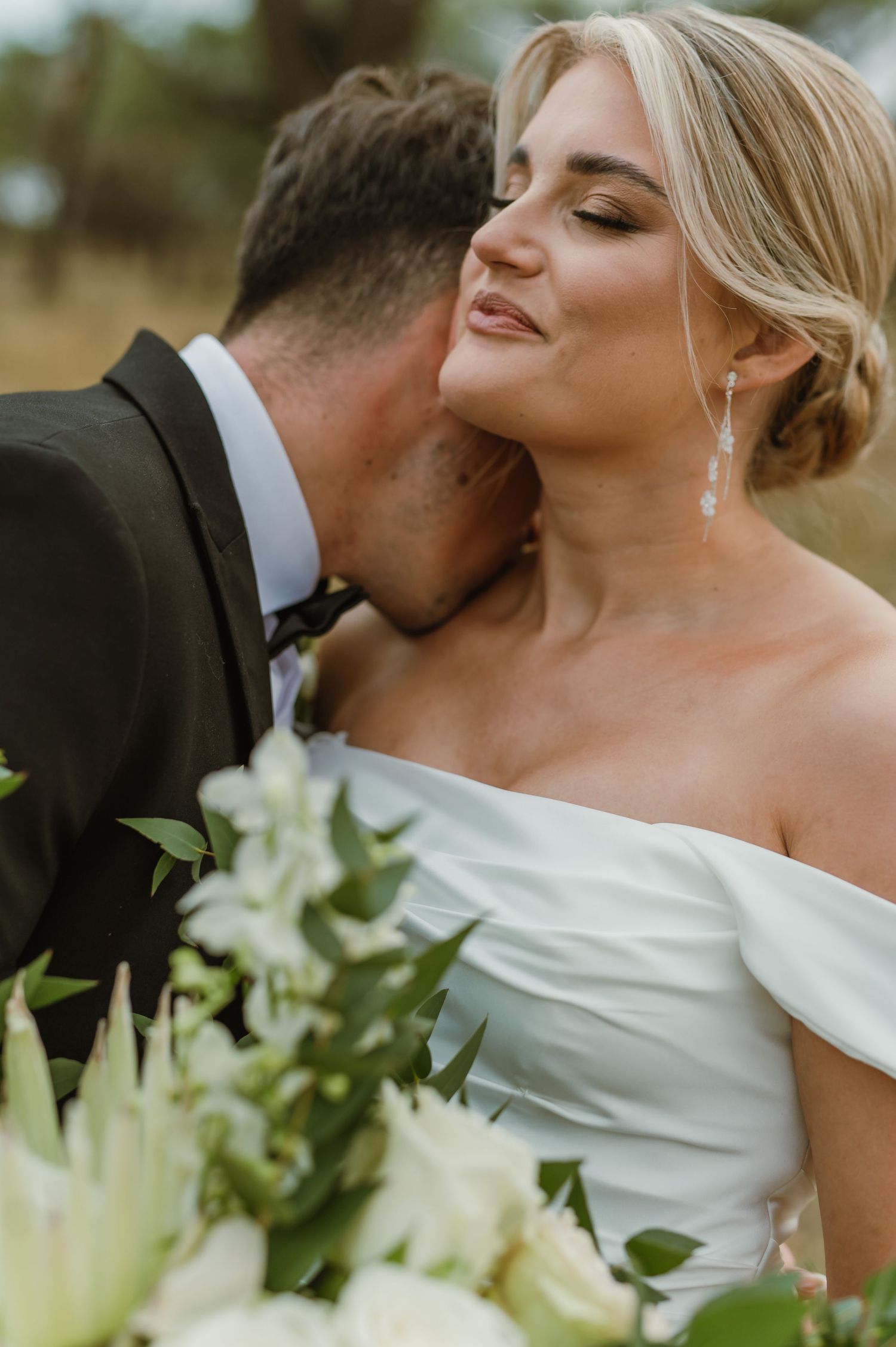 Intimate wedding portrait with white floral bouquet against natural outdoor backdrop.