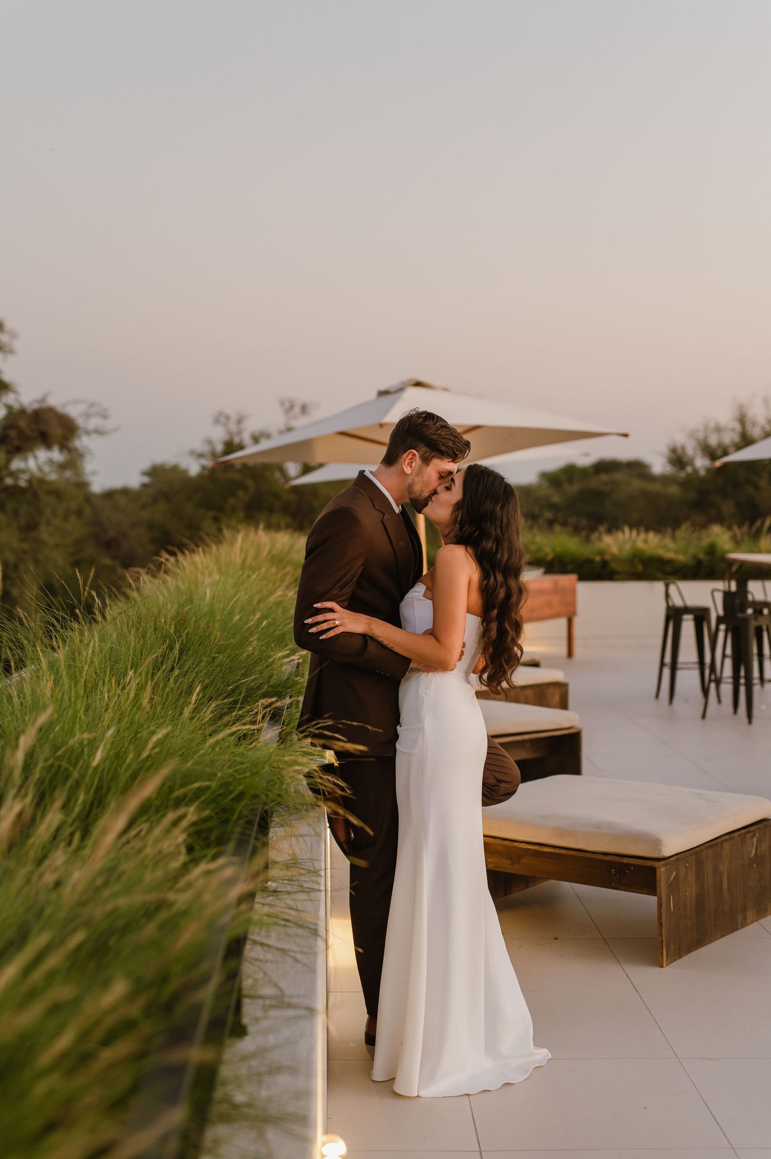 Newlyweds embrace on modern rooftop terrace with natural scenery in background.