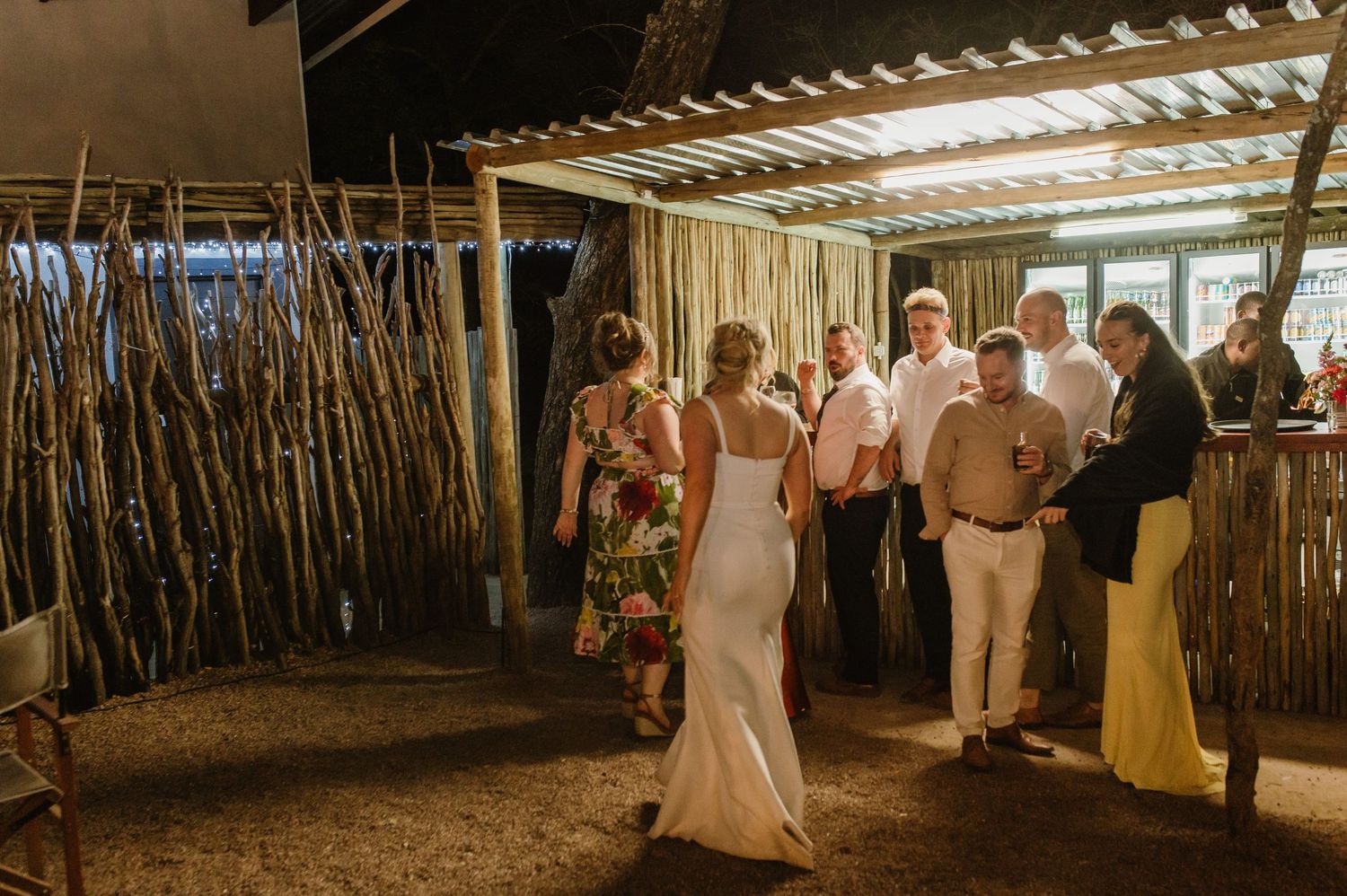 Wedding celebration in a rustic outdoor venue with bamboo walls and evening lighting.