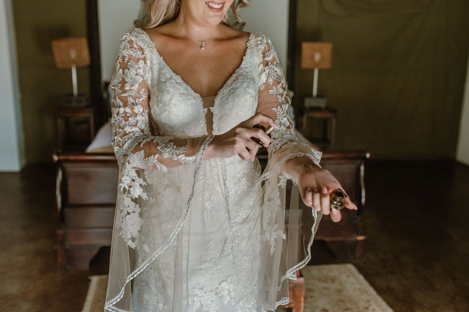 A detailed view of an elegant lace wedding dress with sheer long sleeves in a dimly lit room.