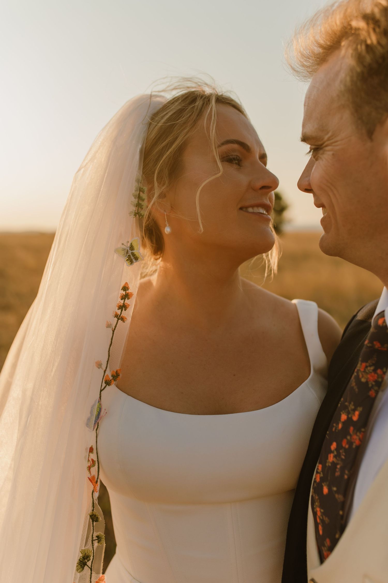 An intimate wedding portrait captured in warm sunset light with delicate veil details.