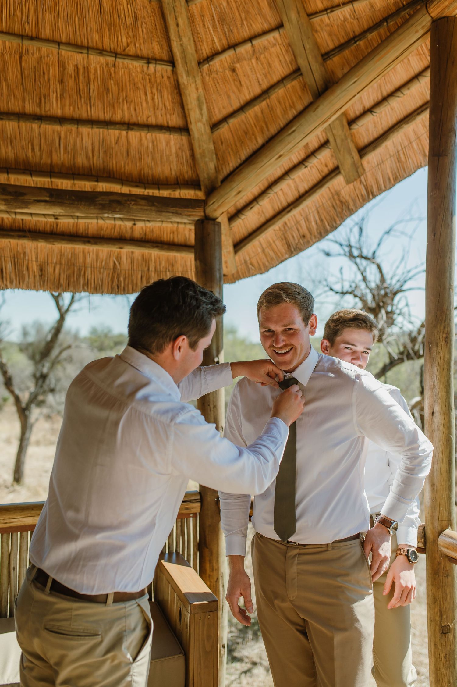 Group helping with tie adjustment in thatched-roof gazebo.