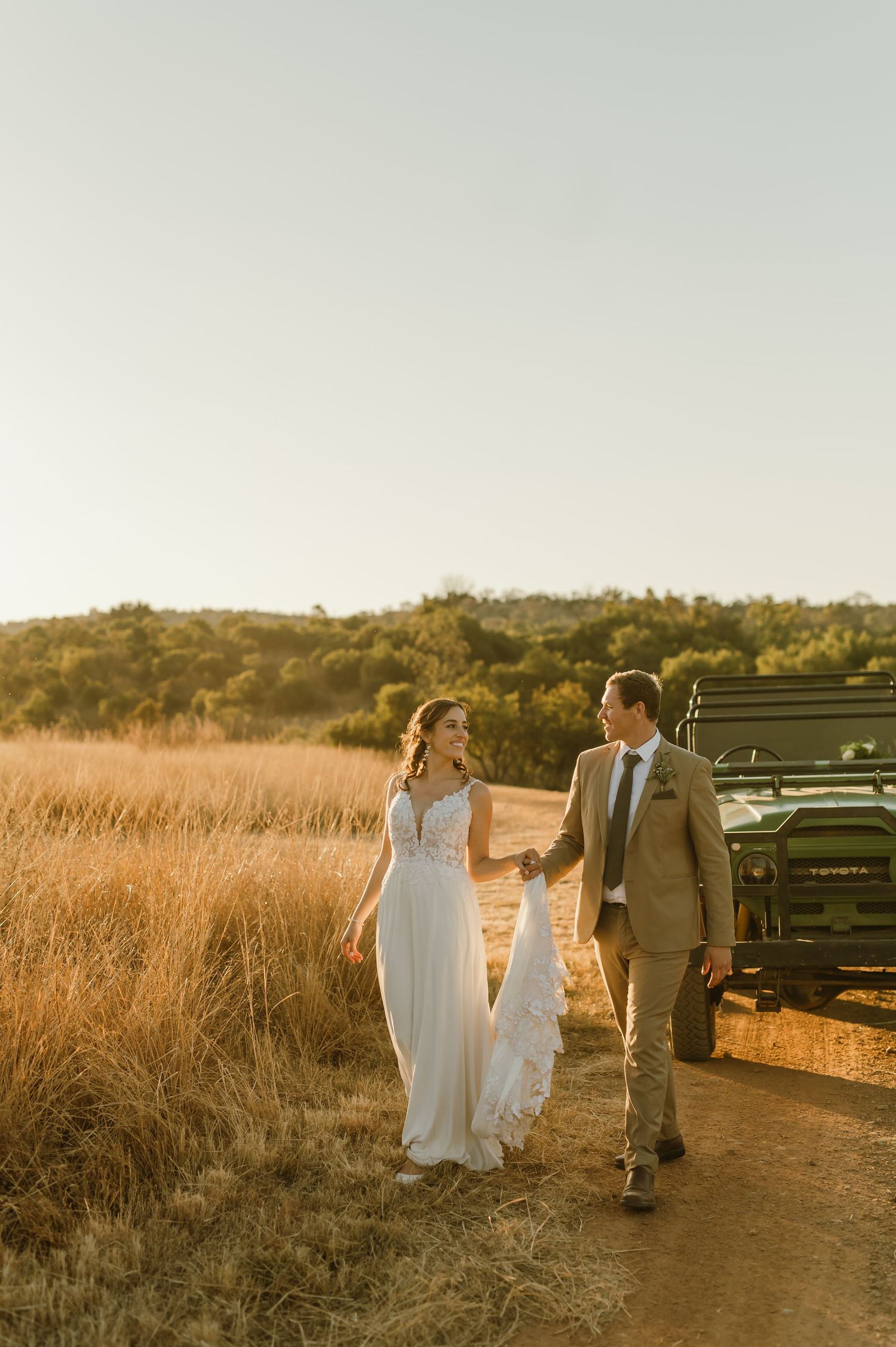 Wedding party walking along a dirt path with tall grass and mountains in the background.