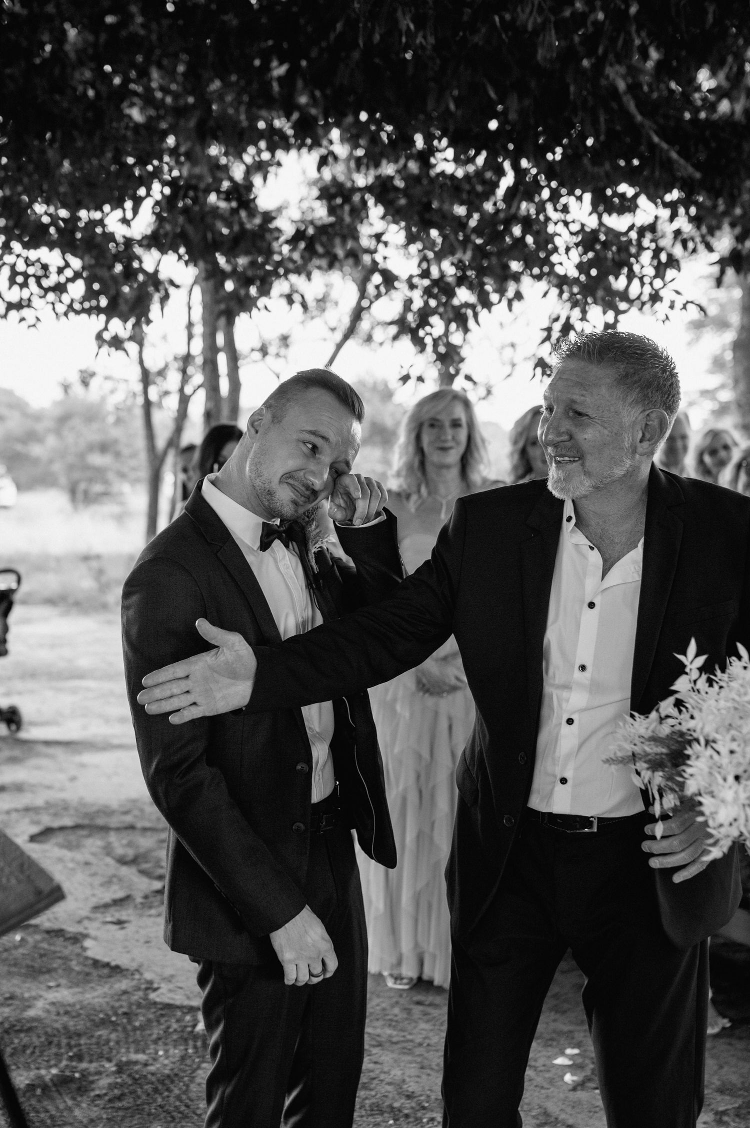 Black and white photo of emotional wedding moment with guests in formal attire.