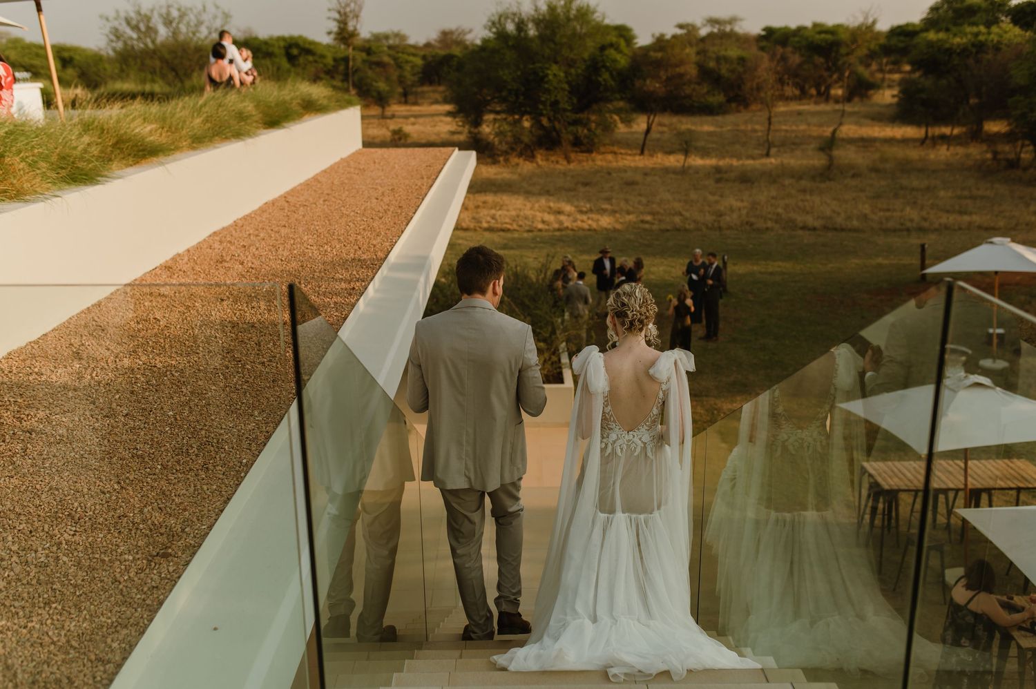 Couple standing on balcony overlooking outdoor wedding venue at sunset.