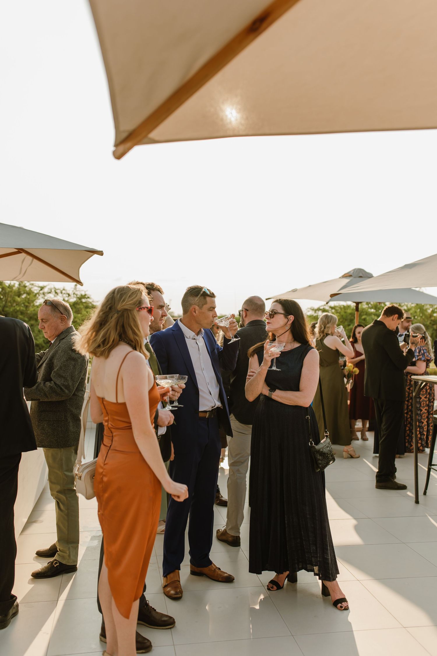 Elegant outdoor cocktail party with guests gathered under cream-colored patio umbrellas.