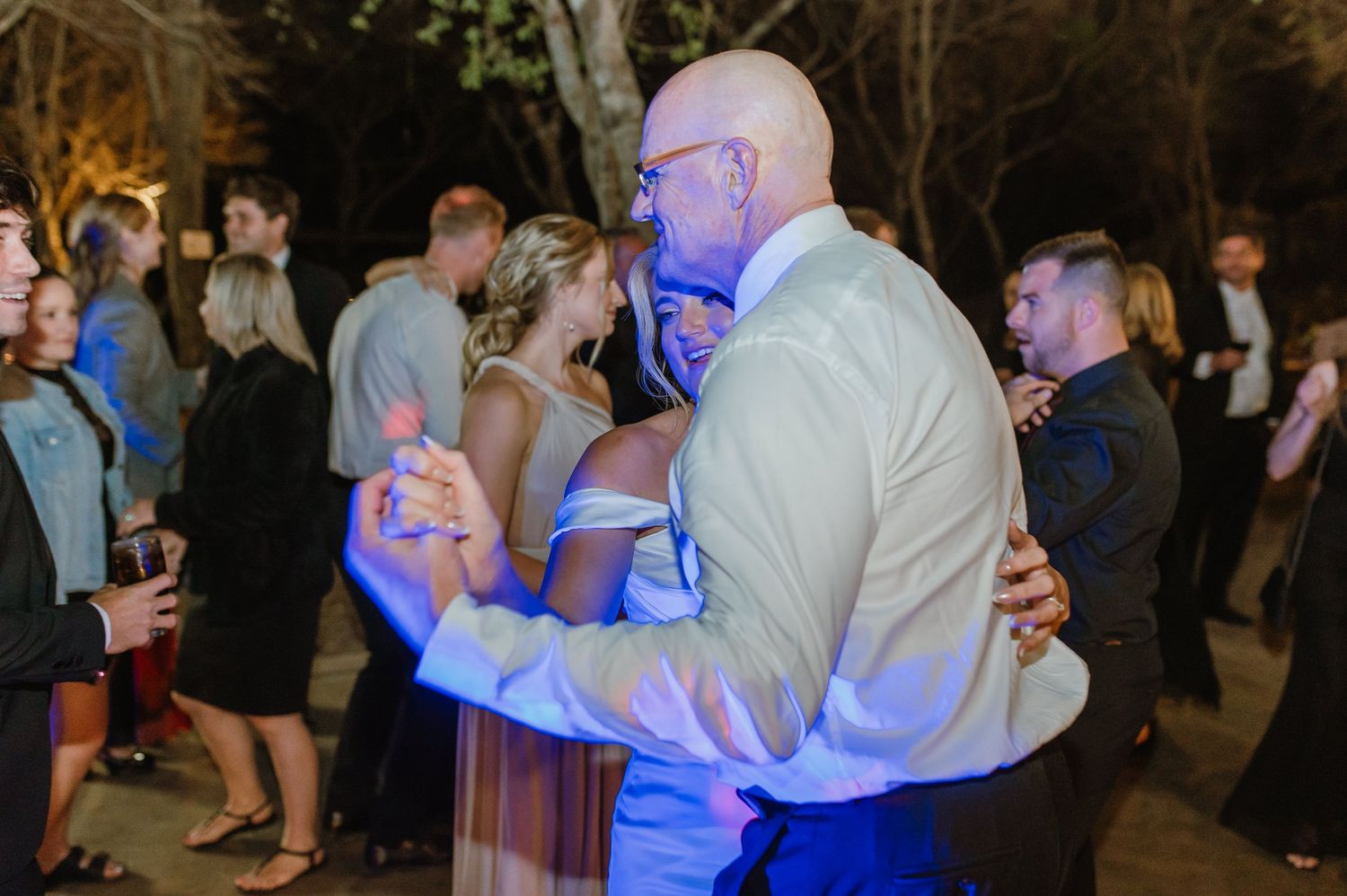 Lively dance floor moments captured at outdoor wedding reception with blue accent lighting.