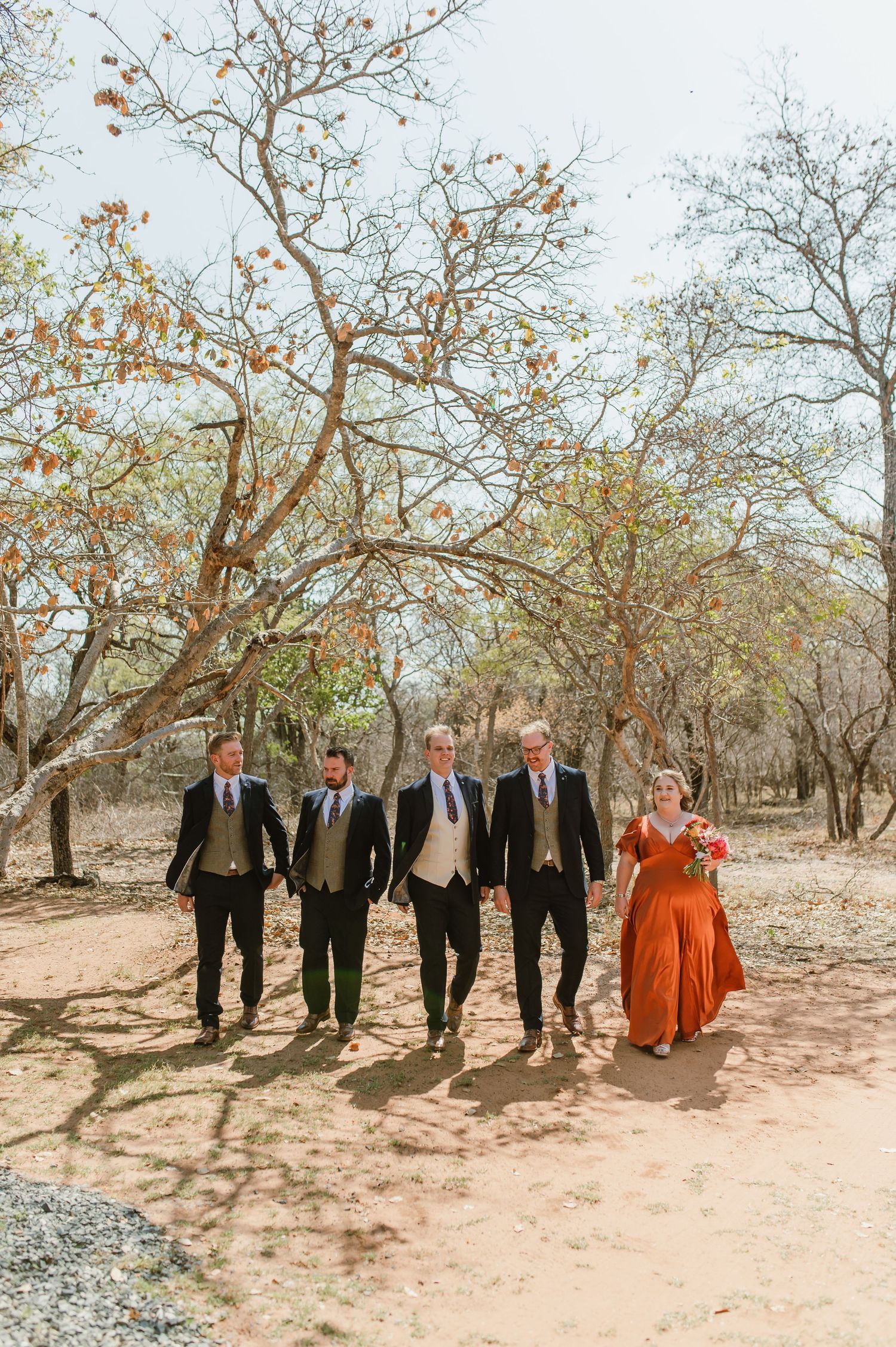 A wedding group walks together through a desert landscape with bare trees overhead.