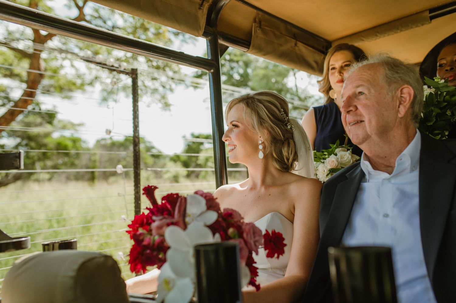 Wedding guests sit in a covered outdoor venue with red floral decorations.
