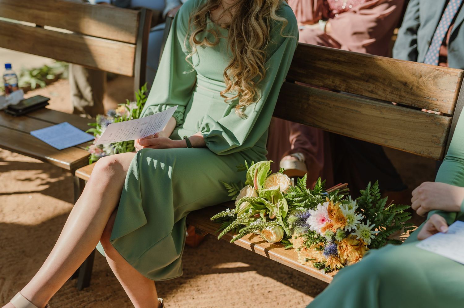Wedding party members in sage green dresses preparing for outdoor desert ceremony.
