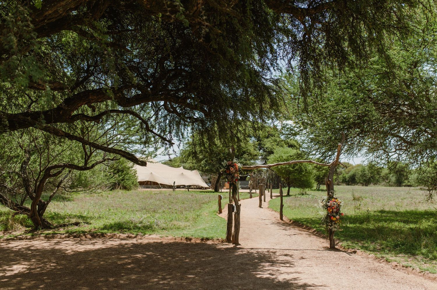 Rustic wooden archway entrance with dirt path leading through lush green trees.