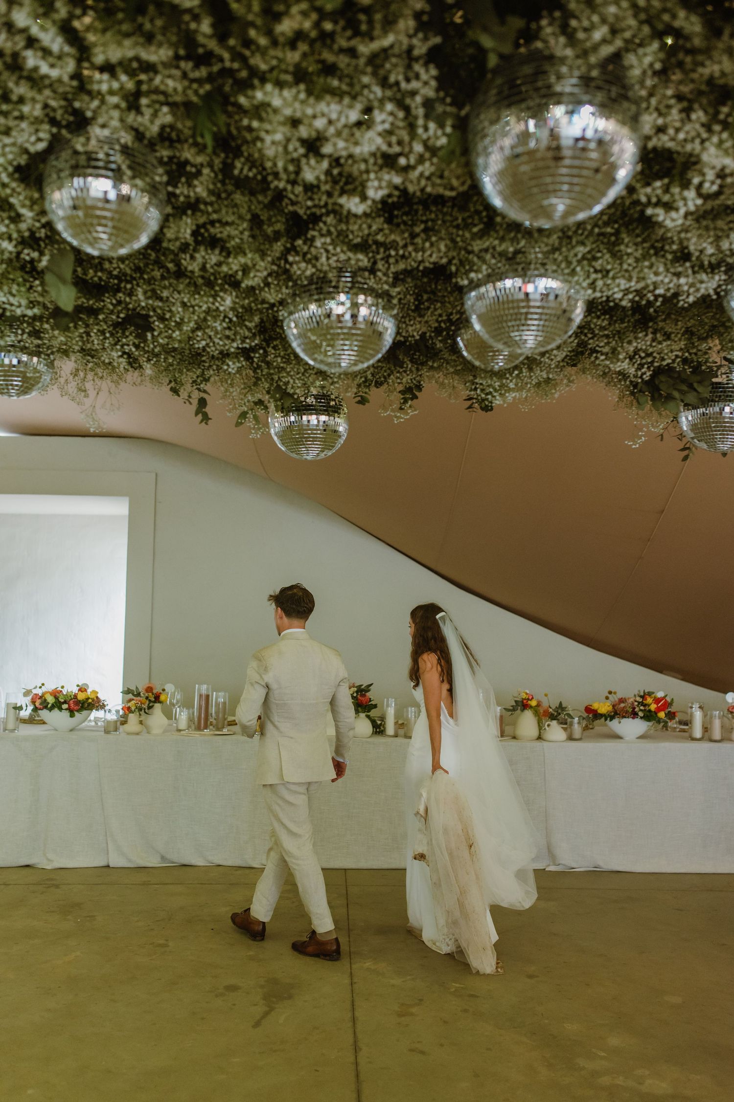 Disco balls and greenery decorate the ceiling of an elegant white wedding reception space.