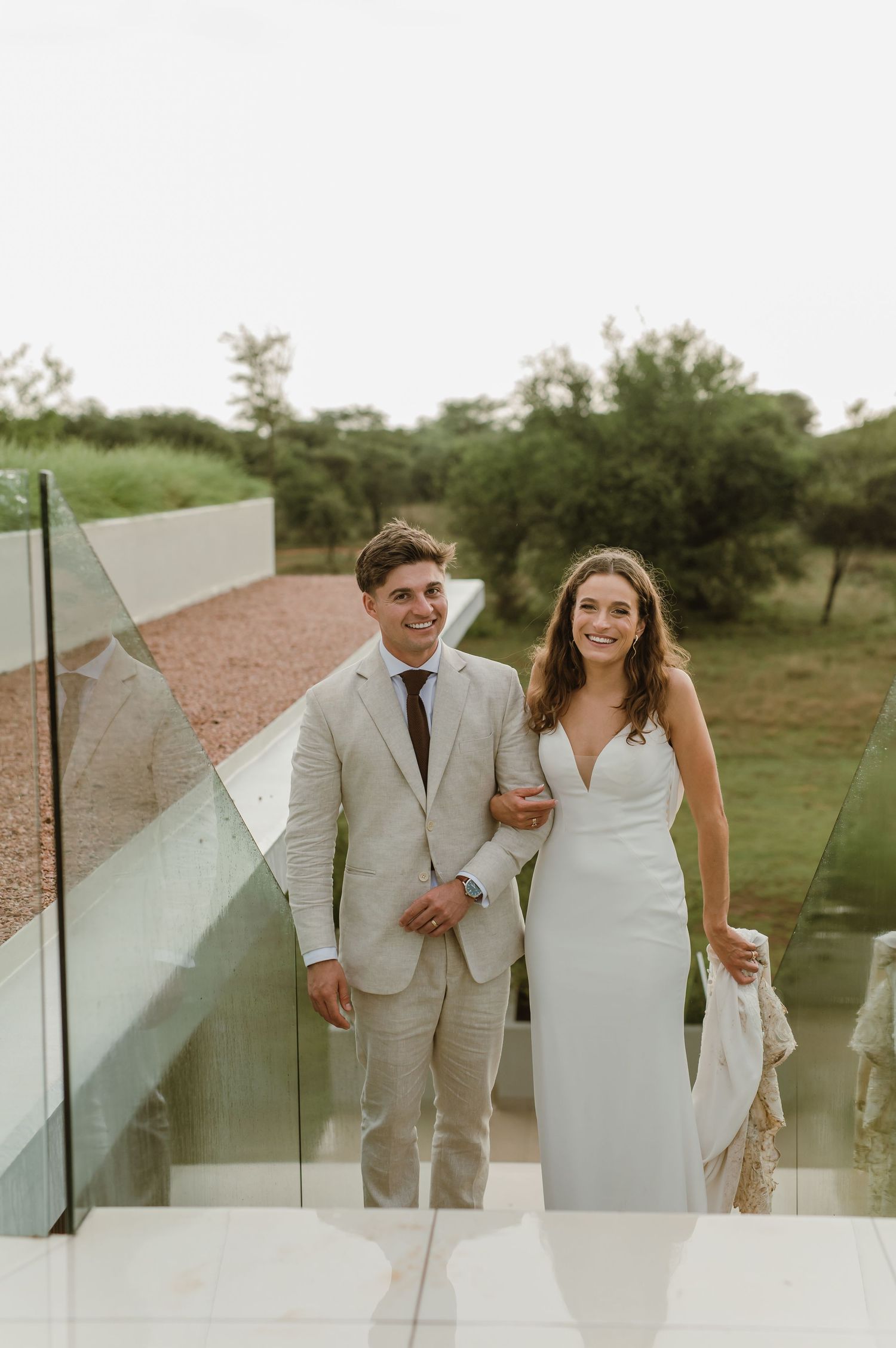 Candid wedding photos showing couple walking and laughing along glass barriers outdoors.