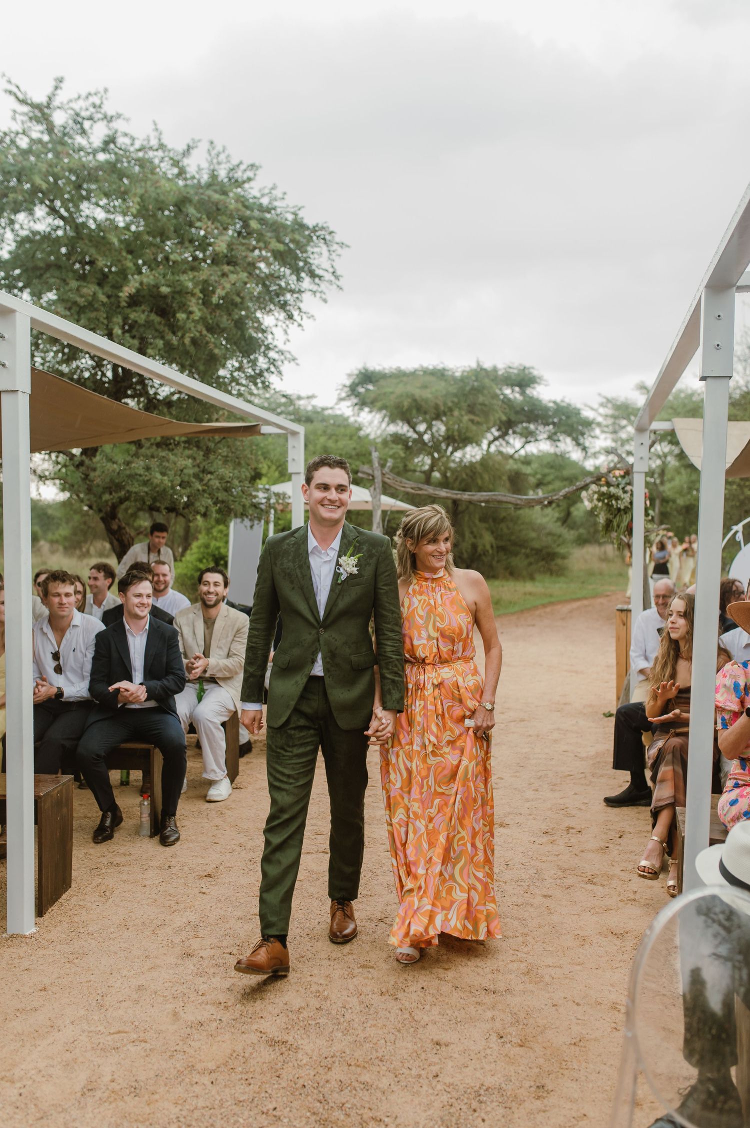 Wedding party members walk down an aisle decorated with white posts on a desert landscape.