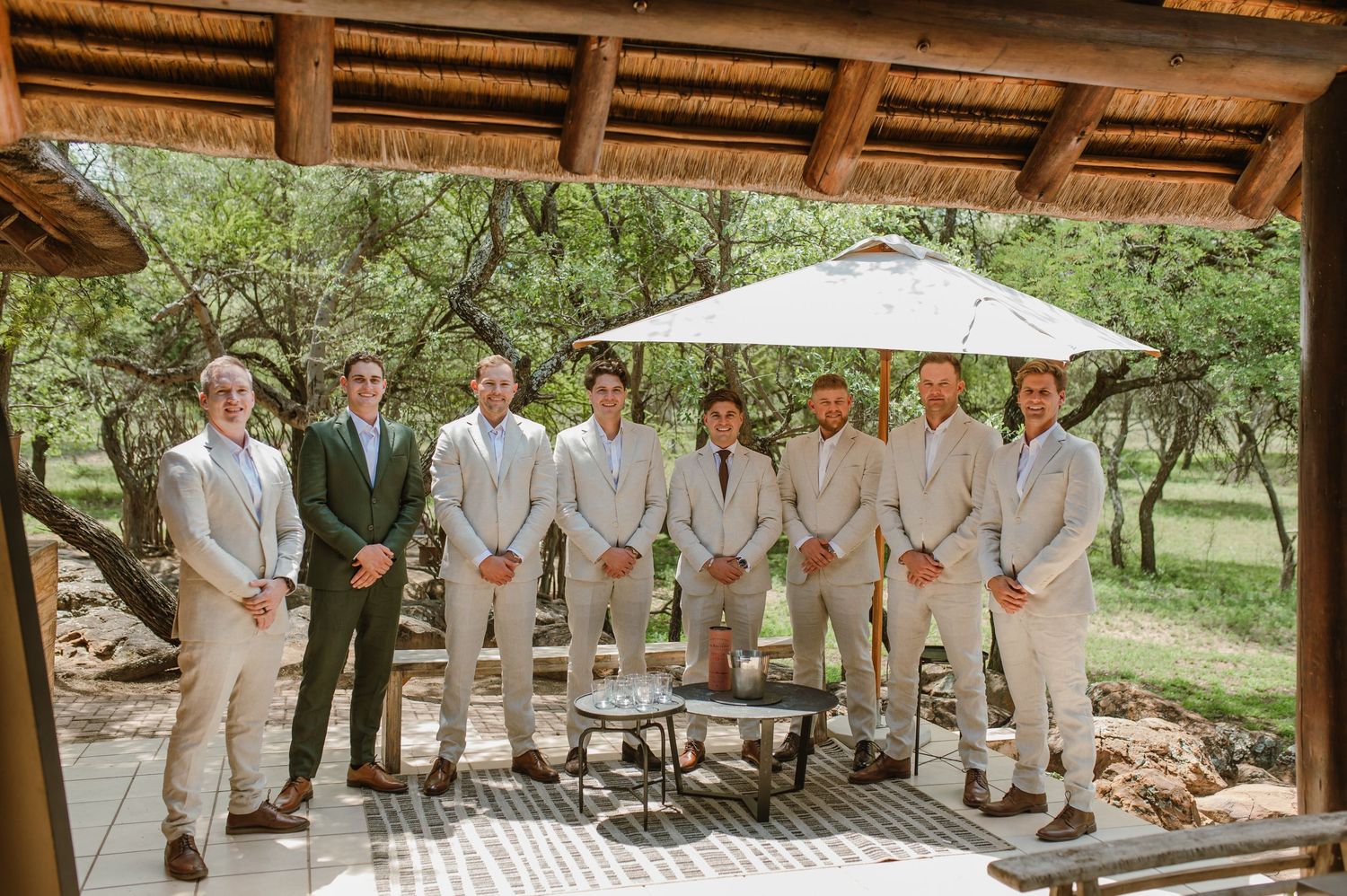 Wedding party in light colored suits gathered under a covered outdoor venue.