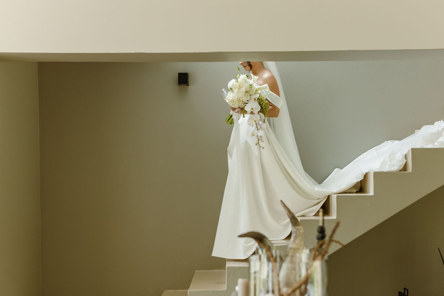 A flowing white wedding dress displayed against a neutral wall in natural light.