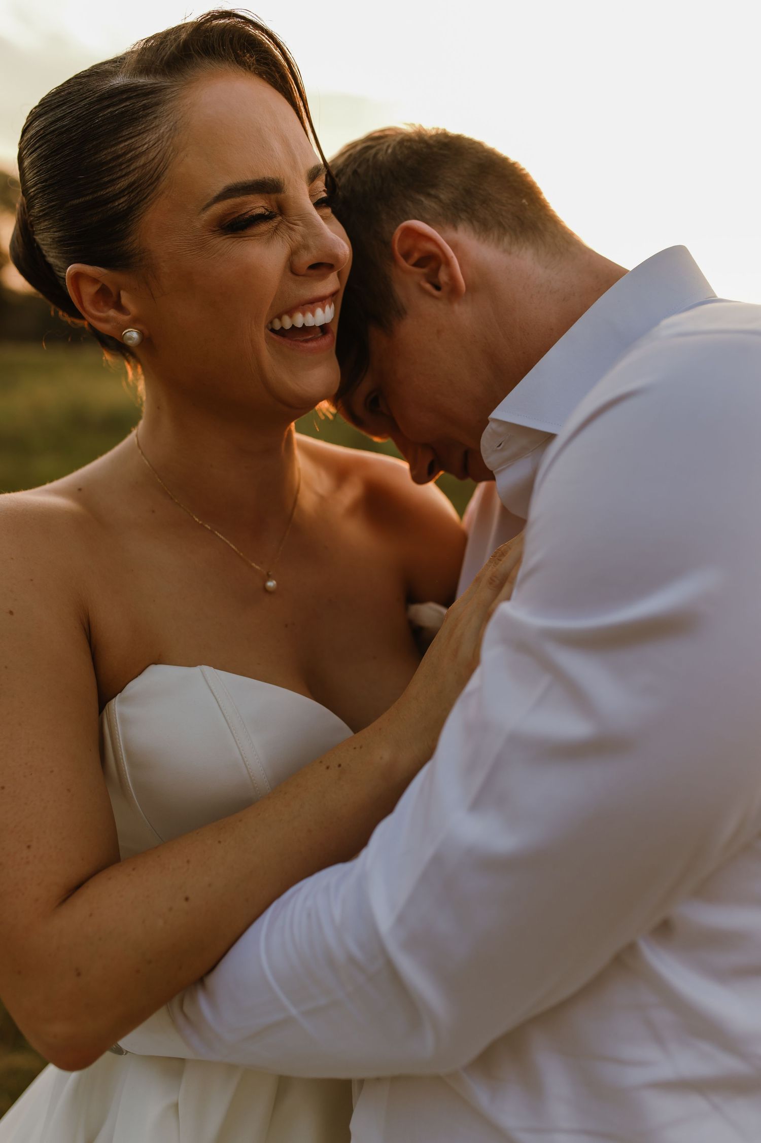 A joyful couple shares an intimate moment during their wedding photoshoot at golden hour outdoors.