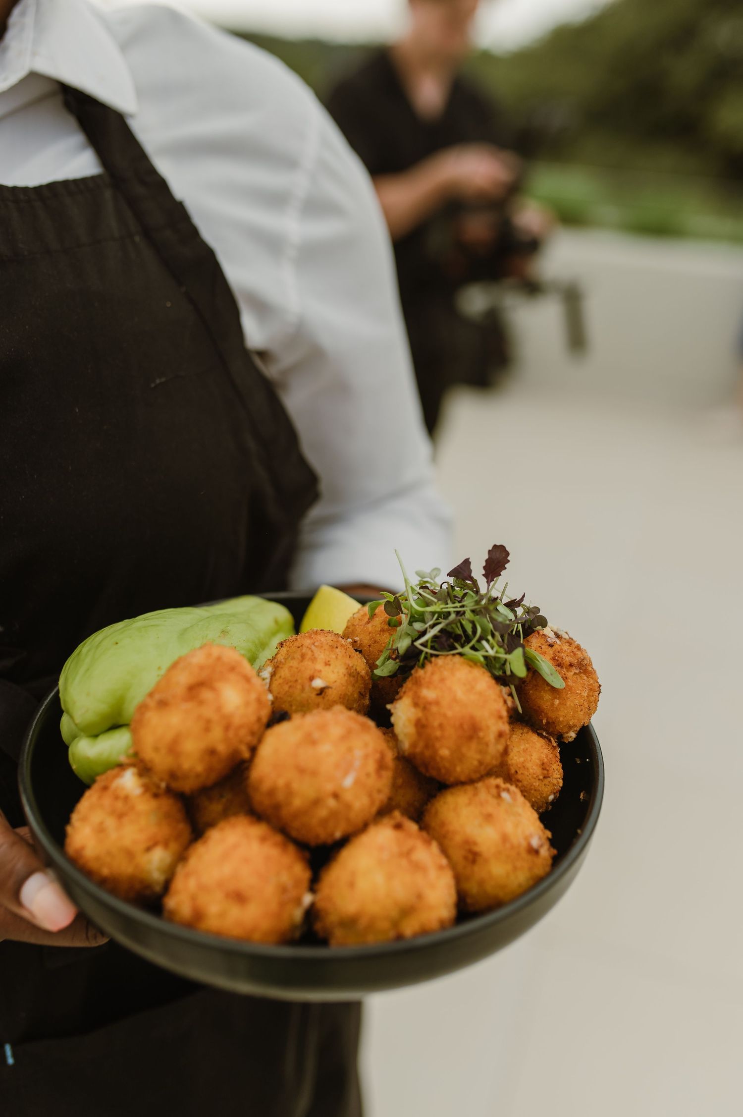 Server holding a plate of golden-brown fried appetizers garnished with fresh herbs.