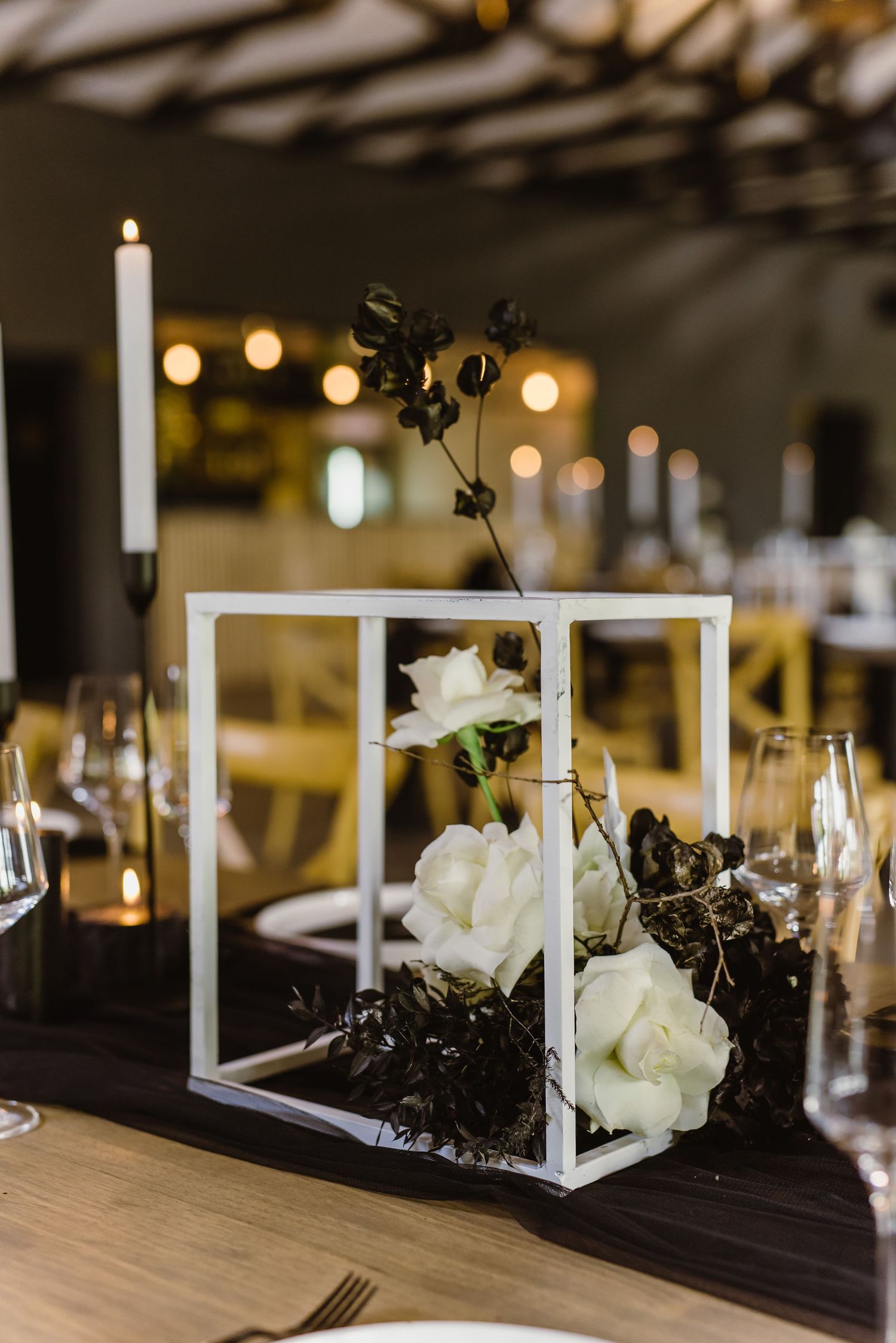 Modern wedding reception table with white geometric centerpieces and candlelight decor.
