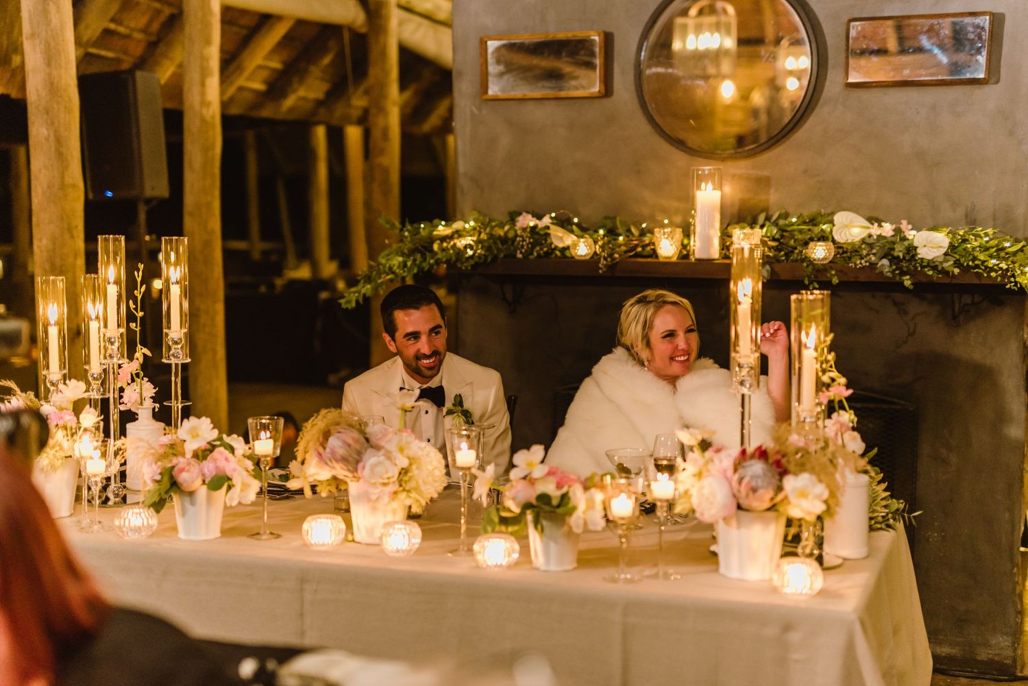 Candlelit dinner tables with white floral centerpieces in an atmospheric wedding venue.