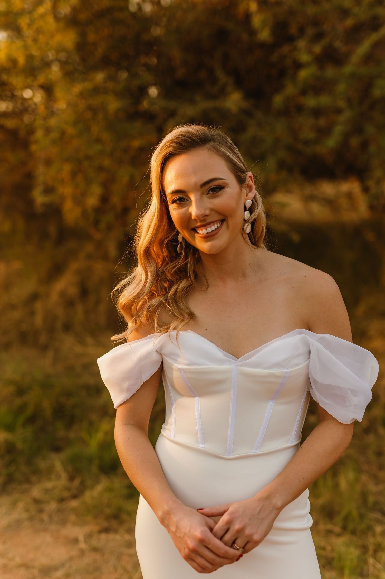 Close-up portrait of someone wearing an elegant white off-shoulder wedding dress in sunset light.