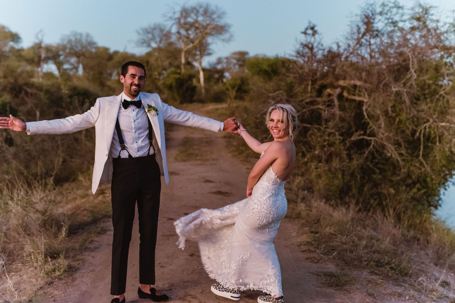 Joyful newlyweds dance and celebrate on a coastal path.