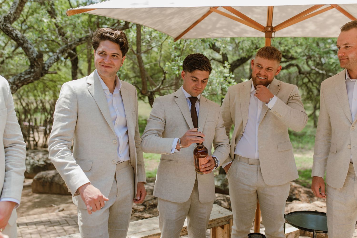 Wedding party members in light suits gather outdoors for pre-ceremony activities.