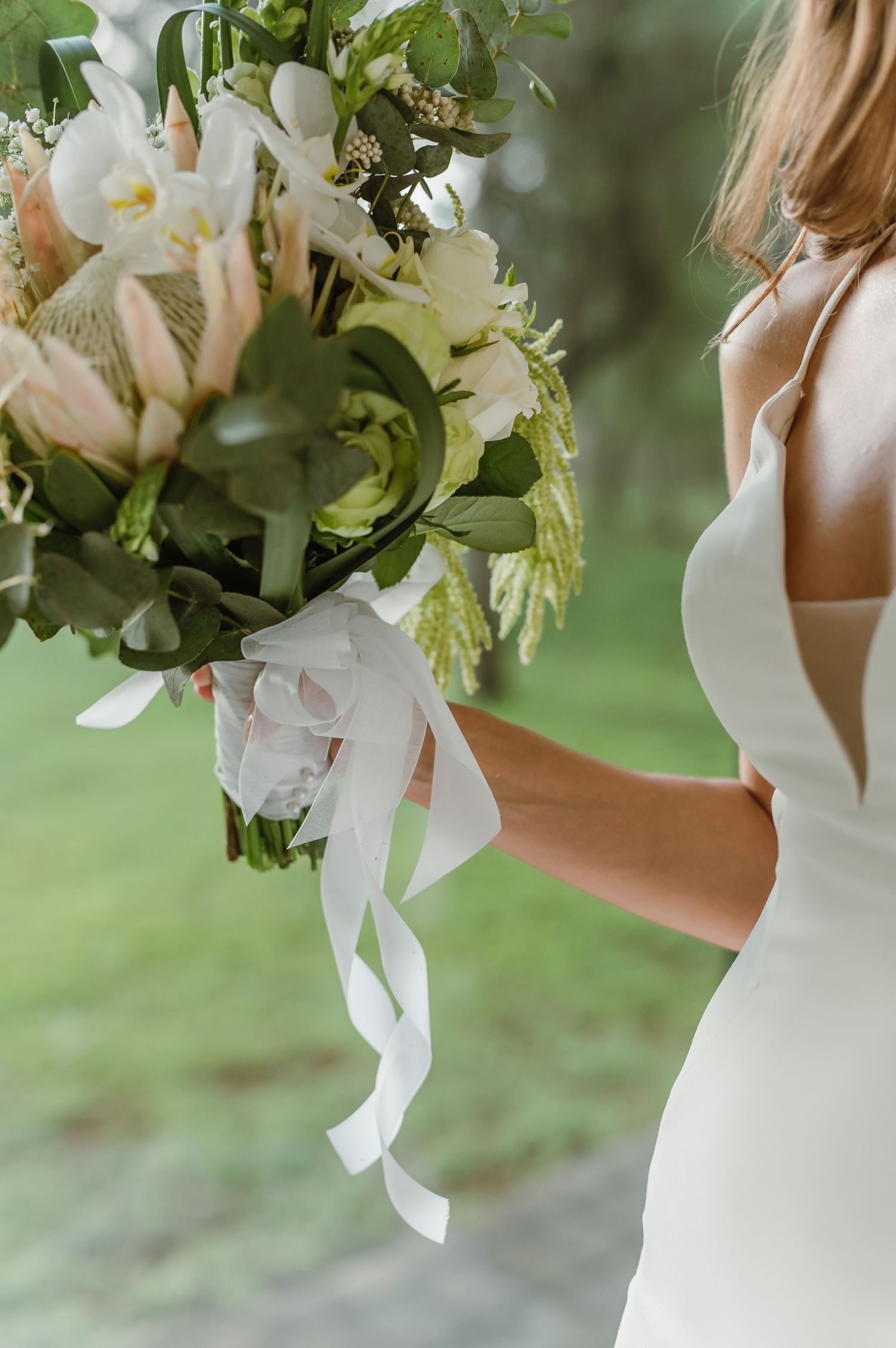Bride holding a lush white and green bouquet against a soft outdoor background.