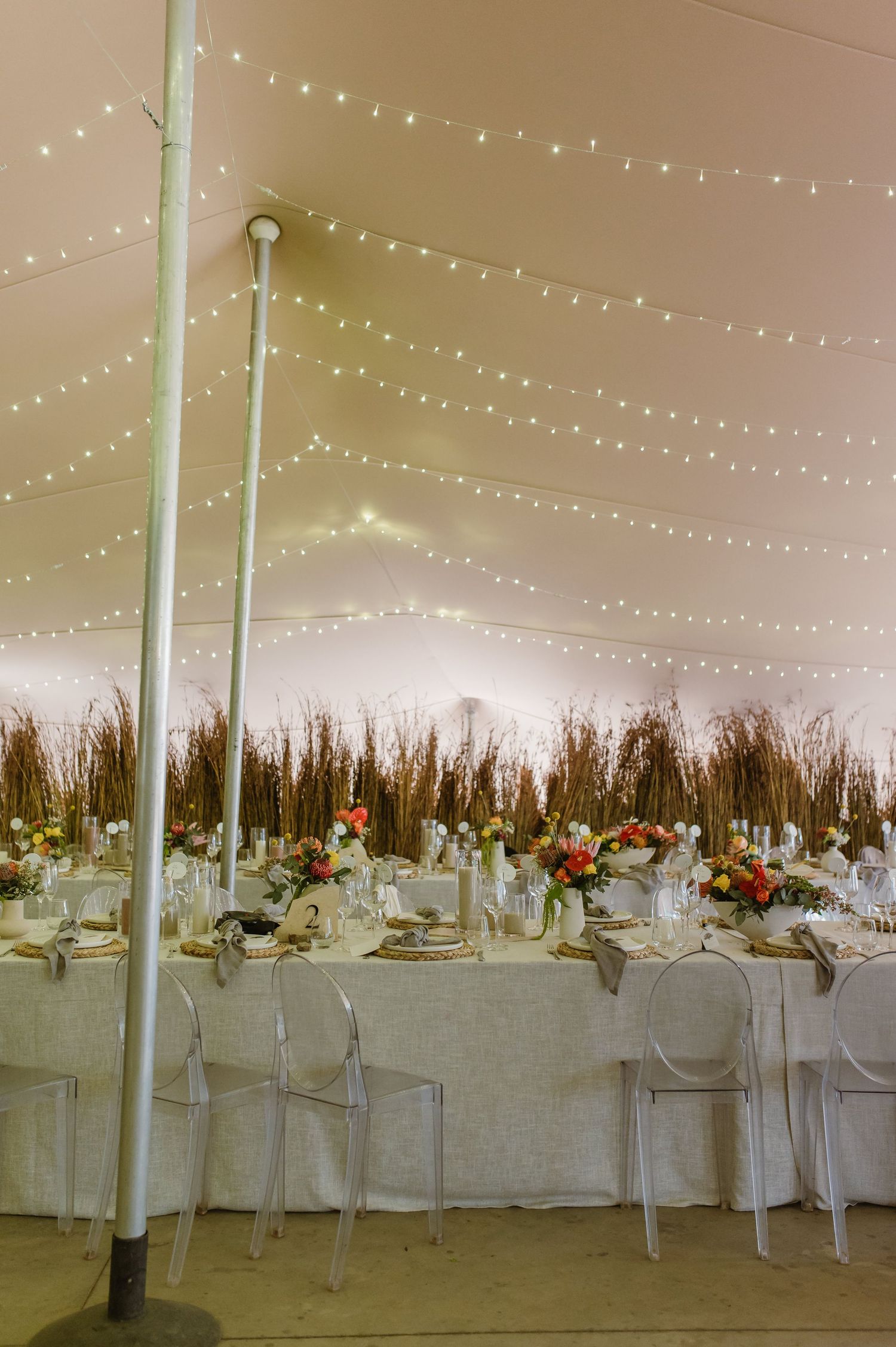 Elegant wedding reception tables set with white linens under string lights in a spacious venue.