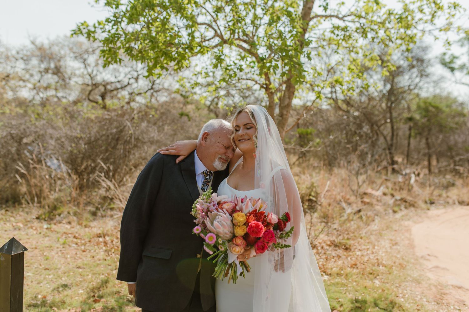 Wedding couple sharing intimate moment under trees in outdoor setting.