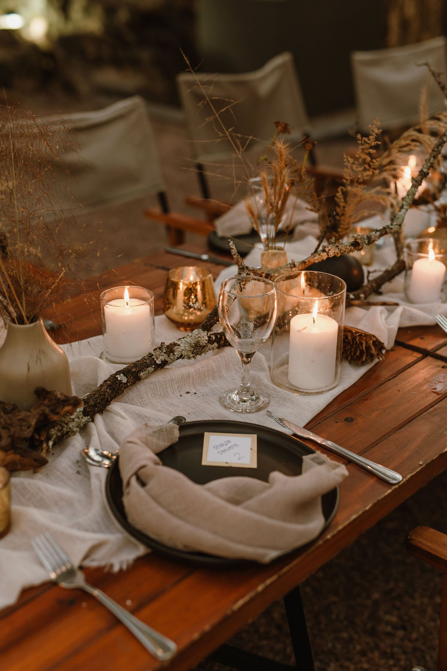 Close-up of elegant place settings with white candles and natural decor on wooden tables.