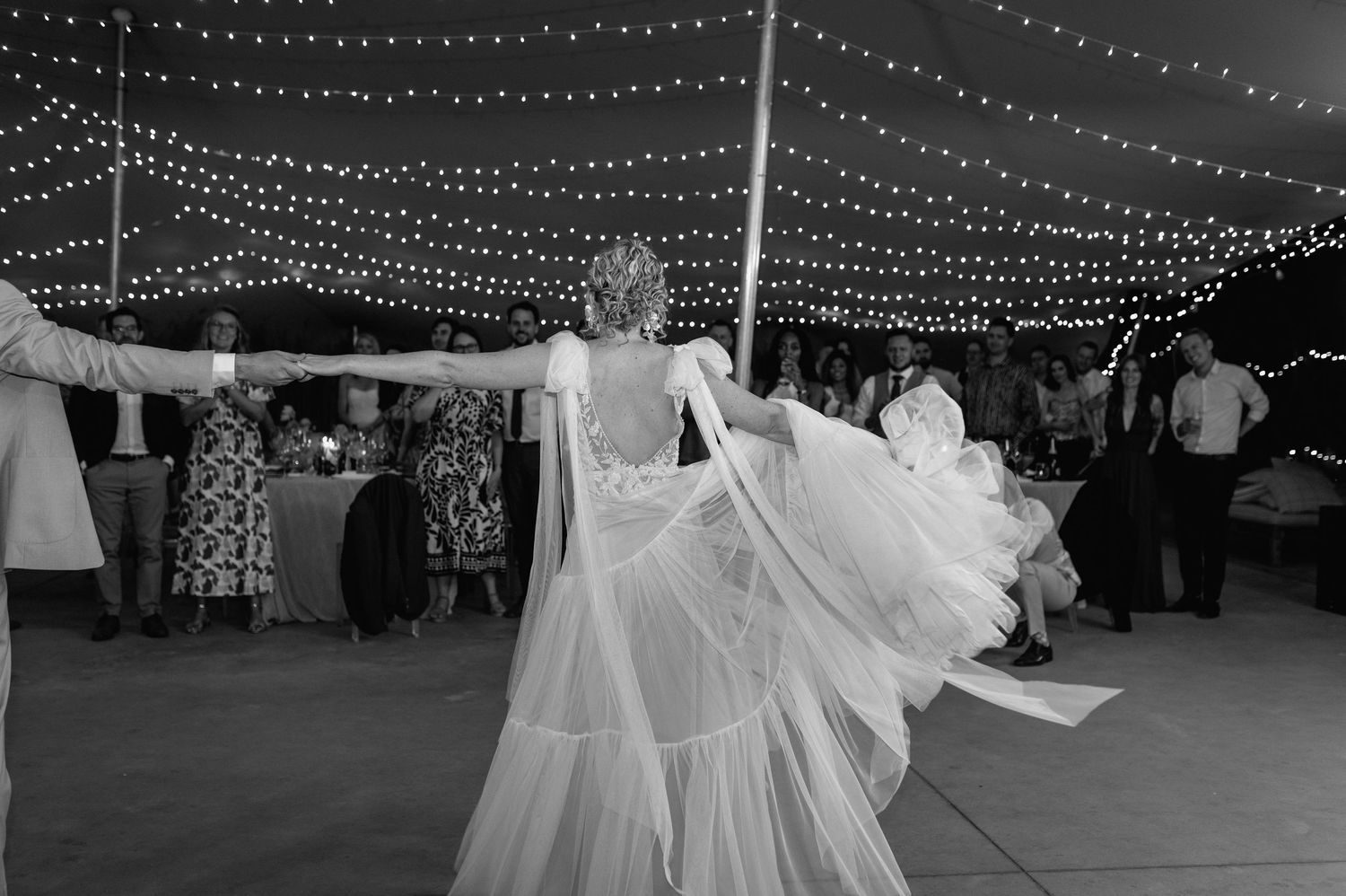 A wedding tent illuminated with string lights and white decor creates a romantic outdoor reception atmosphere.