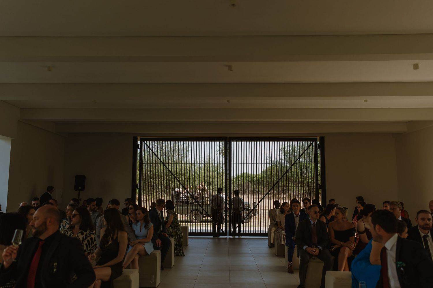 Wedding ceremony guests gather in a modern white room with large windows overlooking desert landscape.