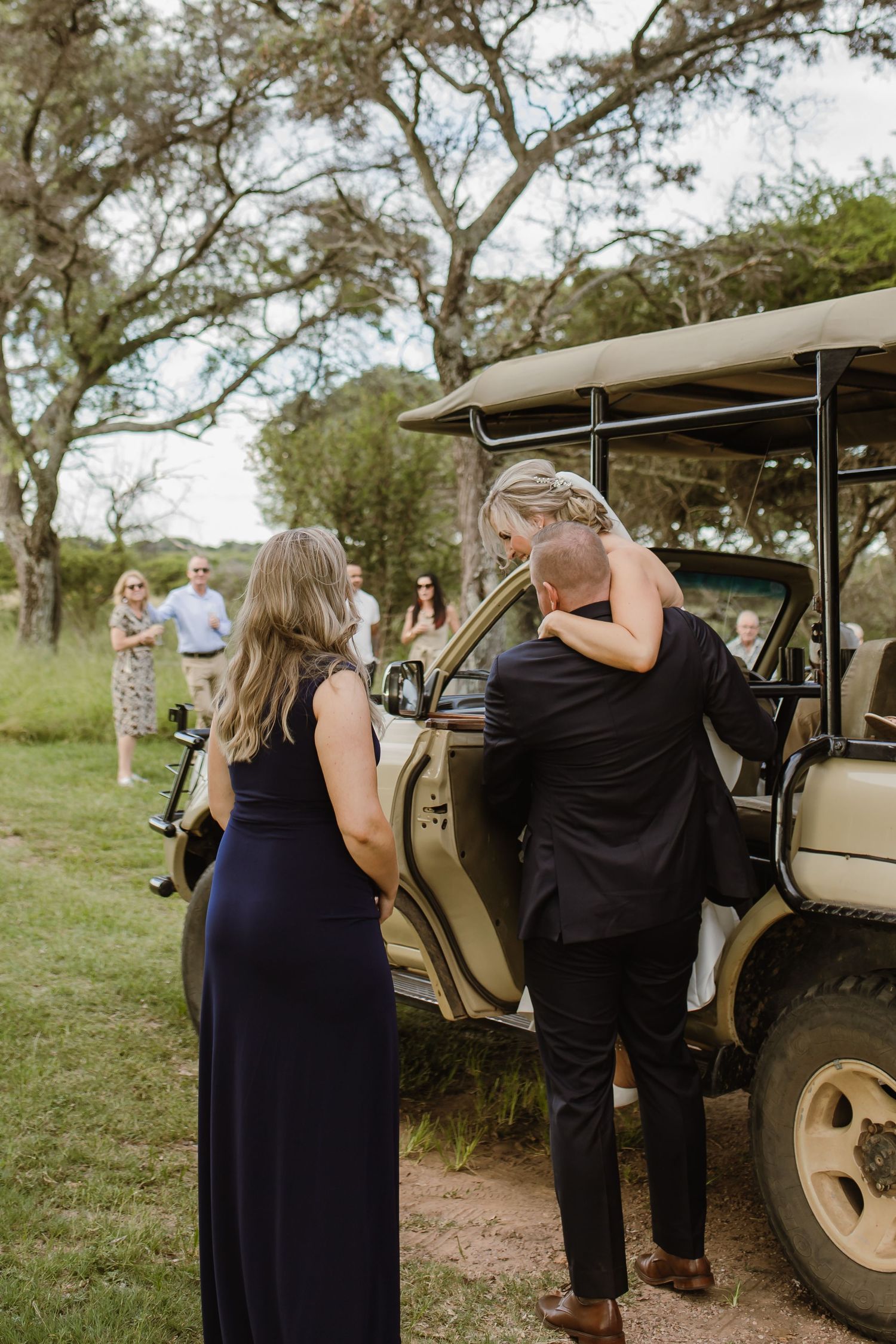Guests arriving at an outdoor safari-style event venue with a parked vehicle in the background.
