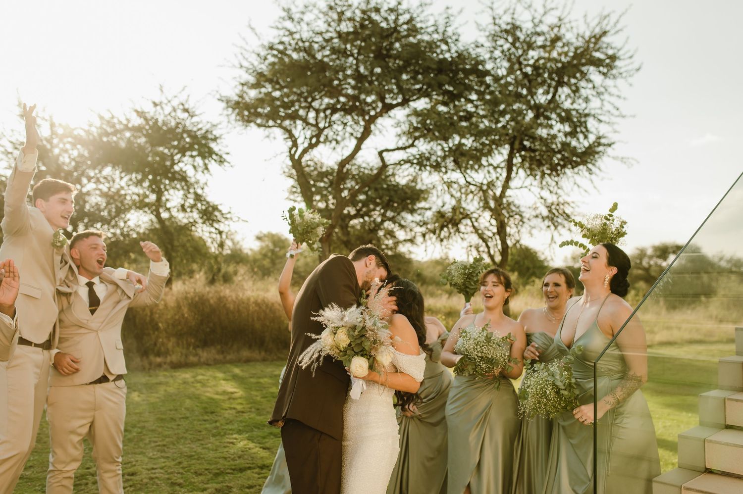 Wedding party poses together outdoors in natural sunlight with trees in background.