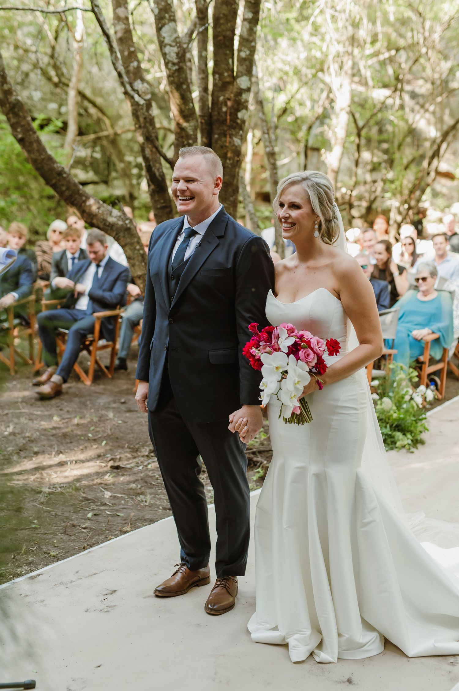 Wedding couple shares joyful moment on forest path during outdoor ceremony.