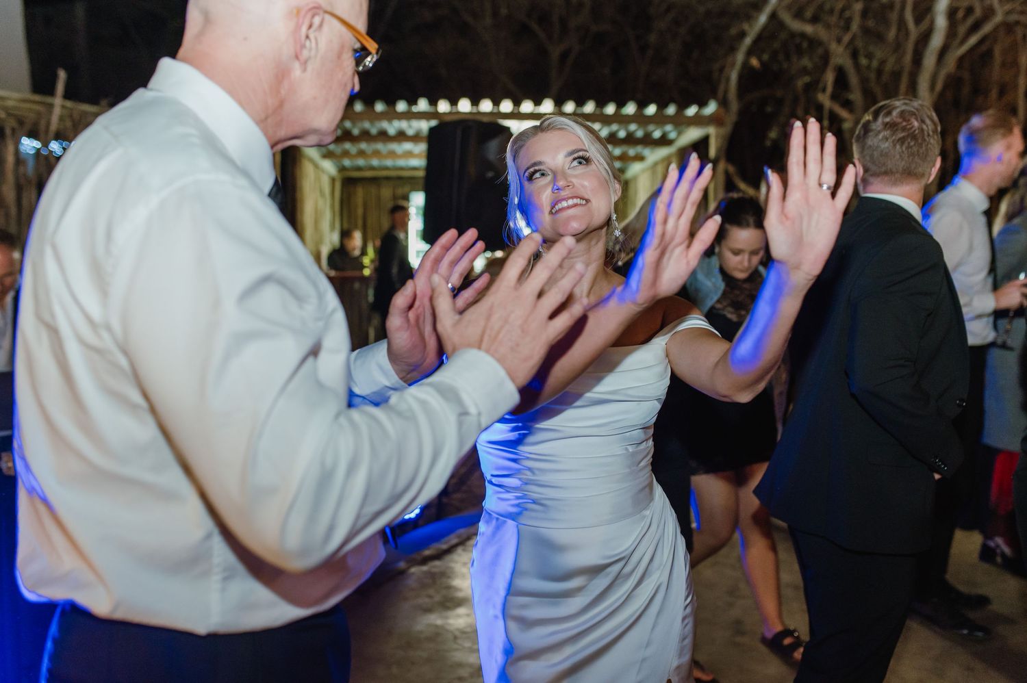 Wedding guests dance together during an evening reception with blue lighting effects.