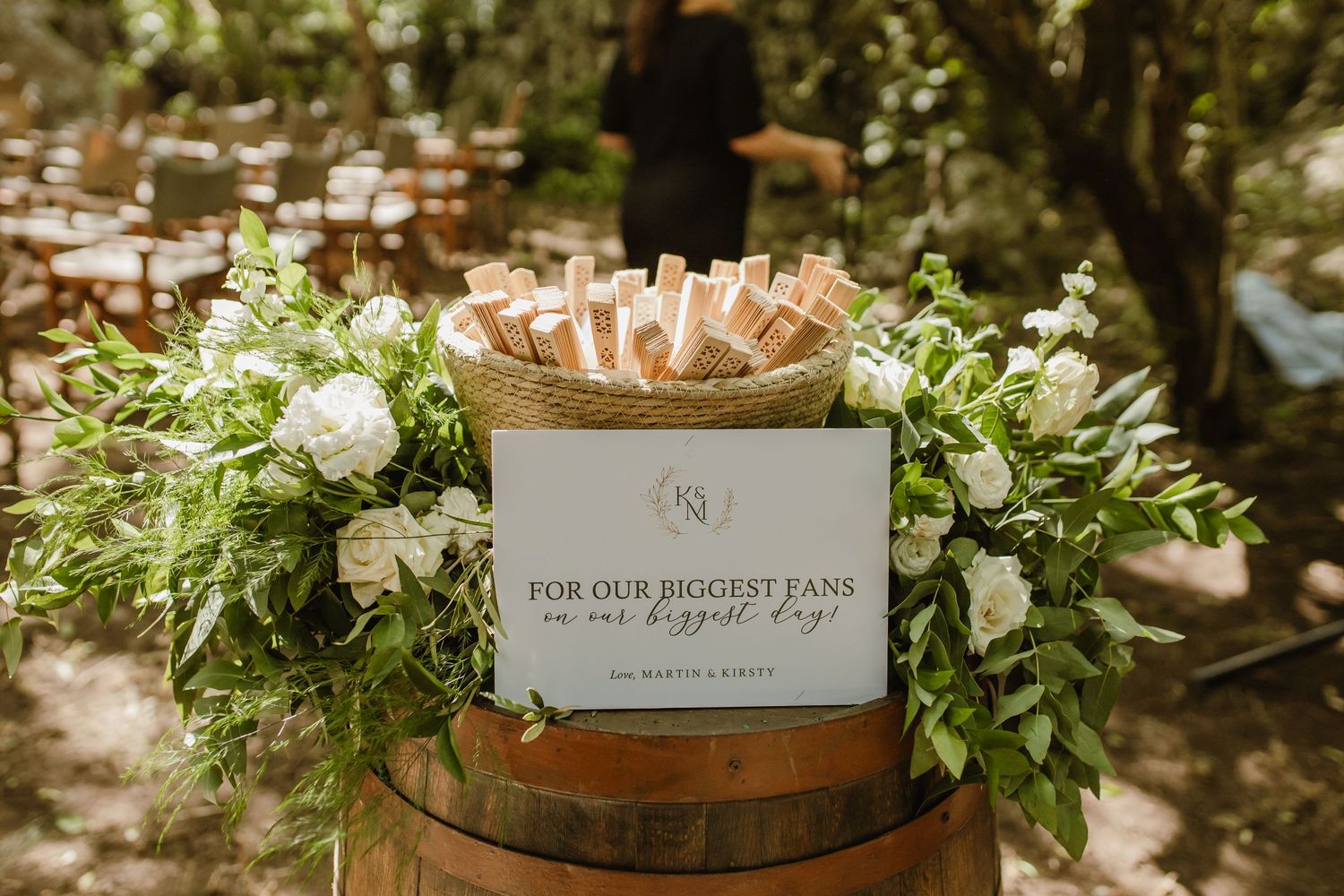 Wedding decorations and greenery adorn wooden barrels in a rustic outdoor setting.