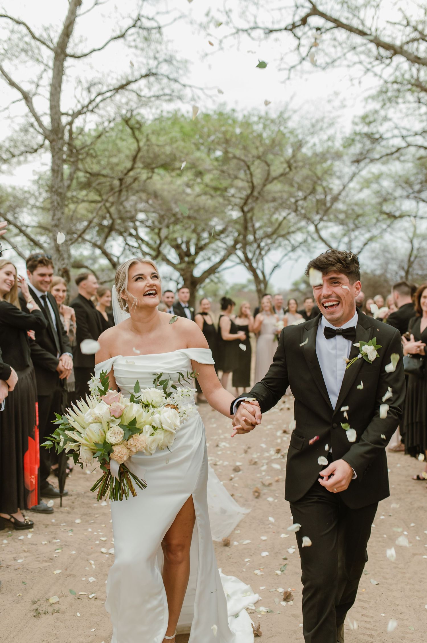 Joyful newlyweds walk down path while guests shower them with confetti.