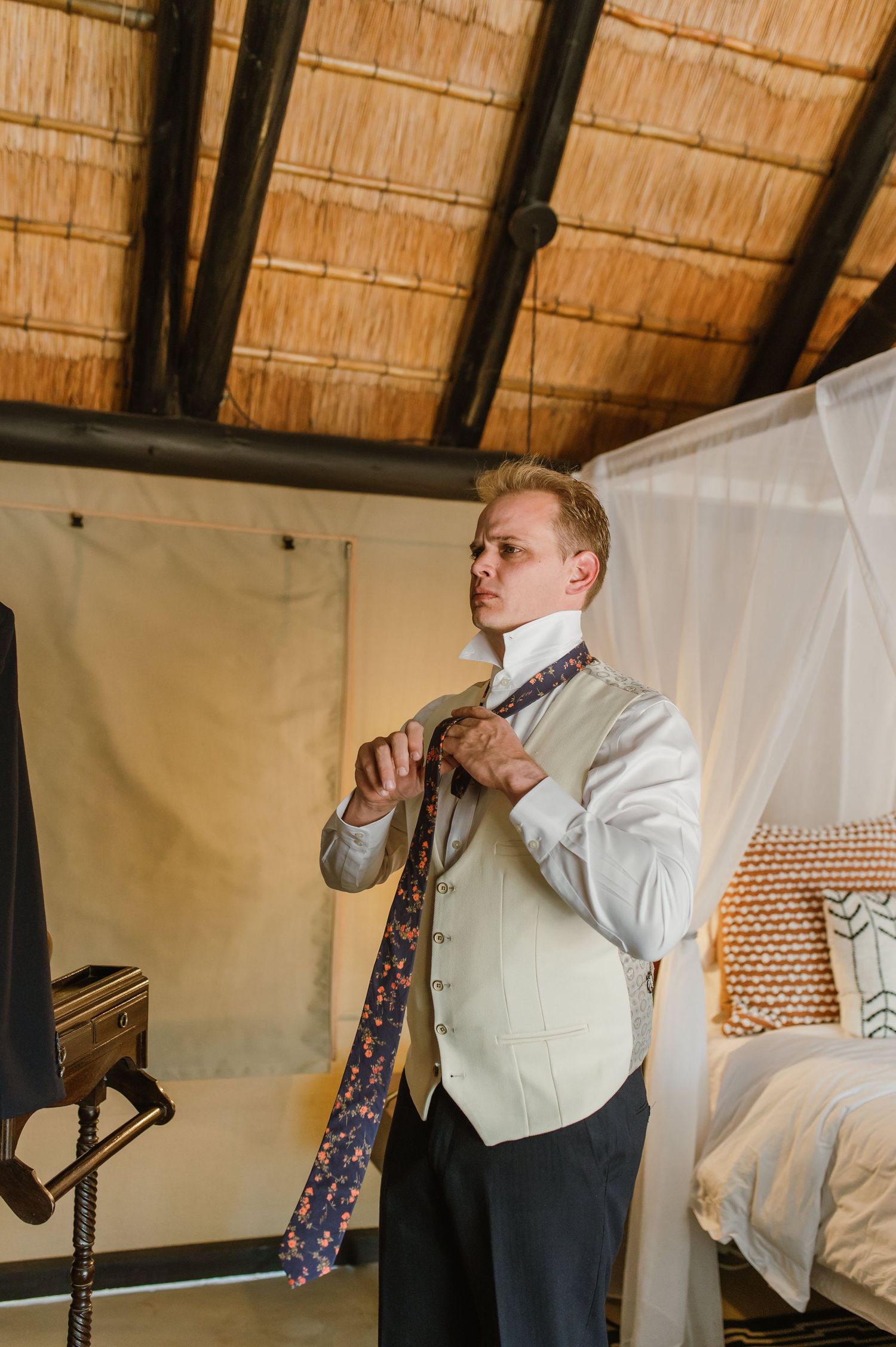 Person selecting a patterned tie while getting dressed in a room with thatched ceiling.